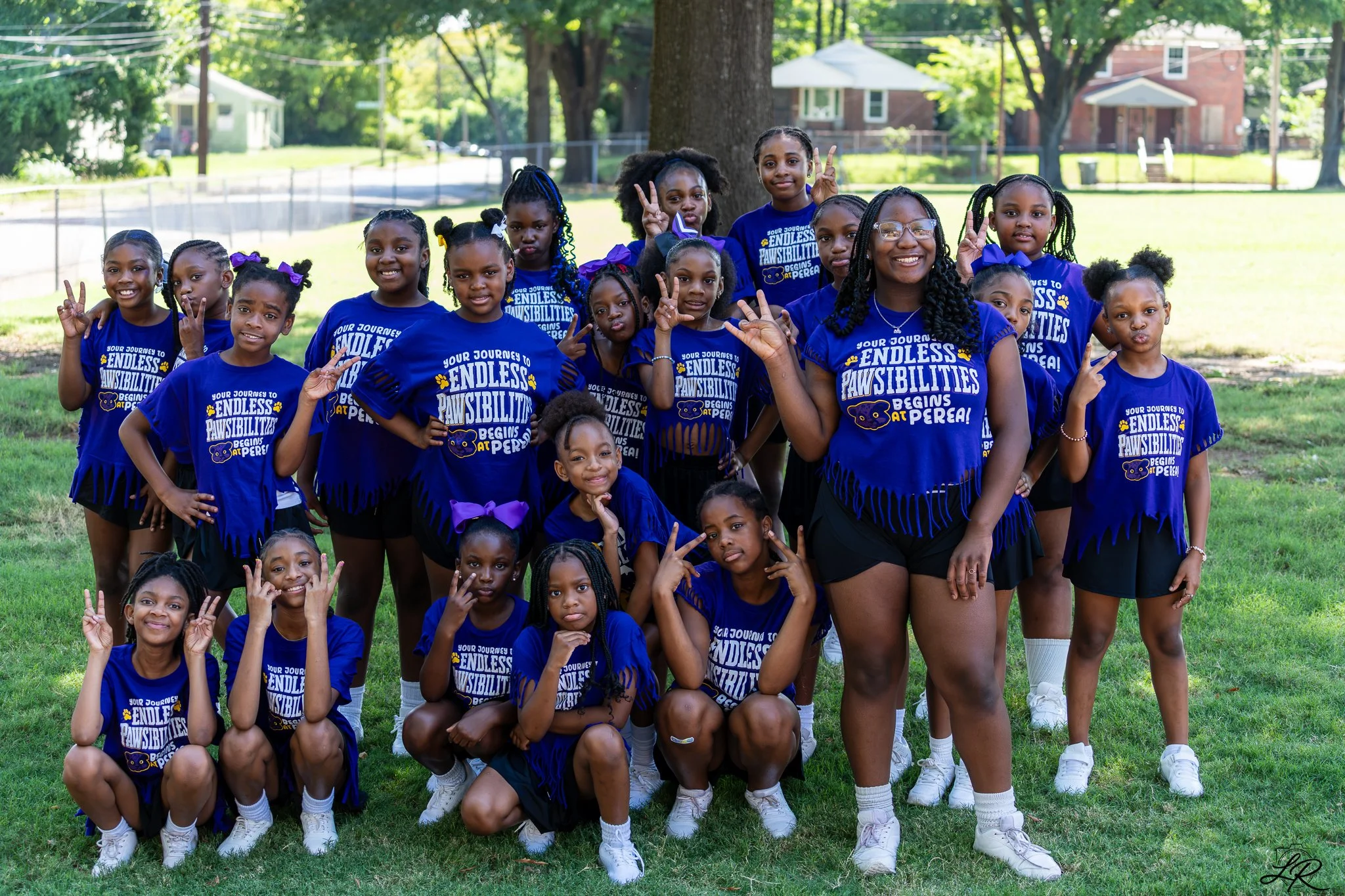 Group of young girls and a woman outdoors in a park, wearing matching blue t-shirts with the phrase 'Endless Pawsibilities' and smile and pose for the photo.