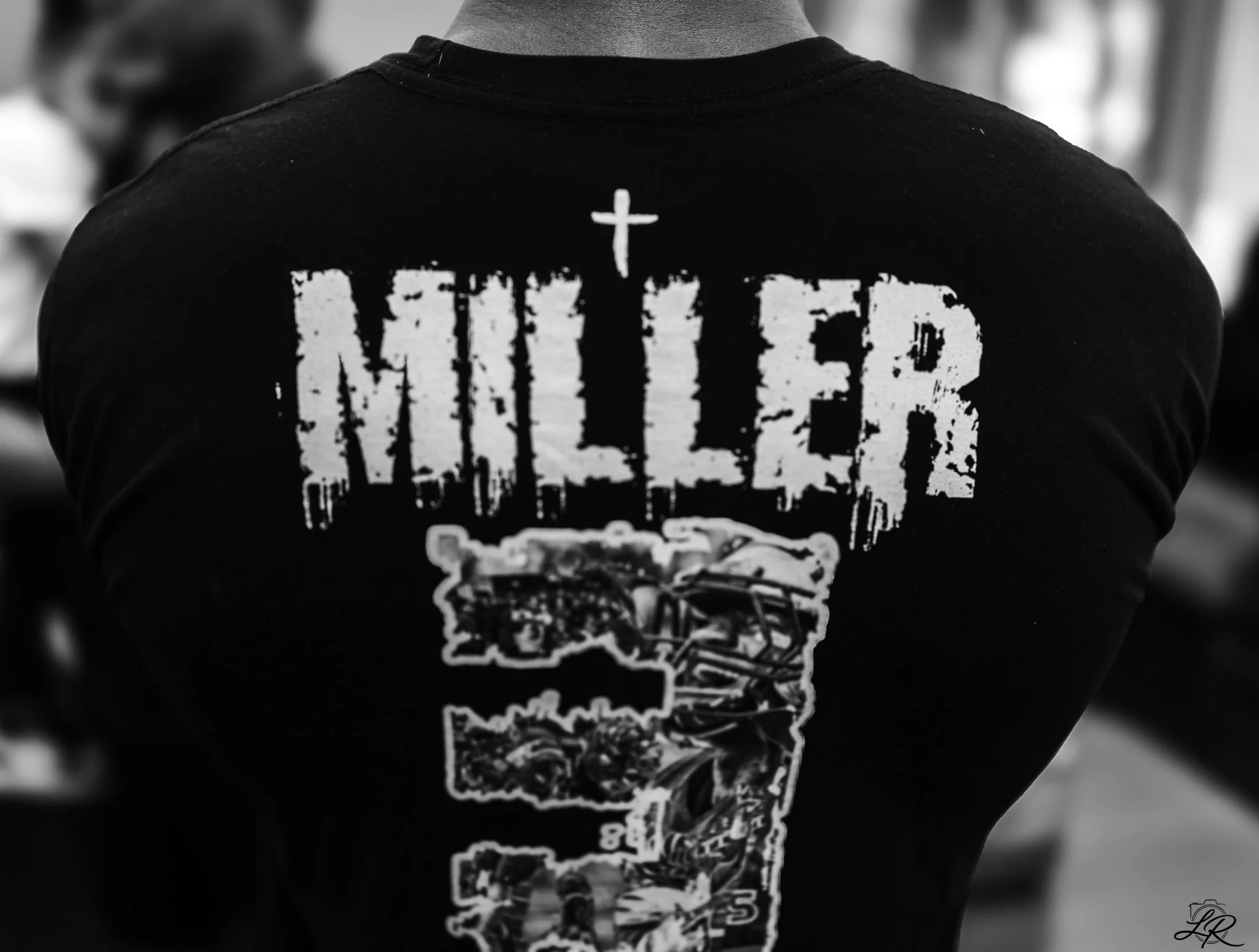A person wearing a black T-shirt with a white graphic design on the back, featuring text and images, viewed from the back.
