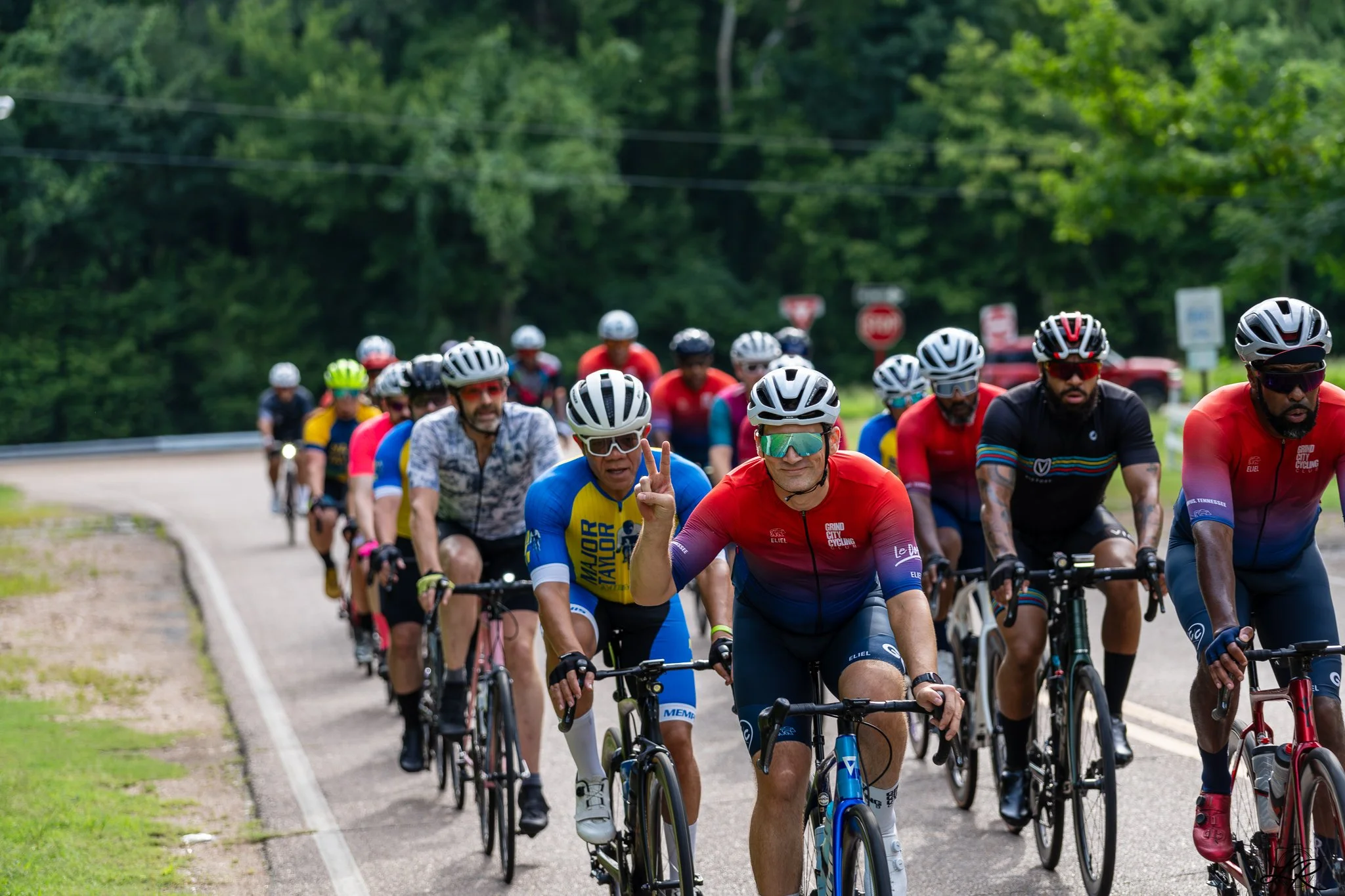 Group of cyclists riding on a road through a green wooded area.