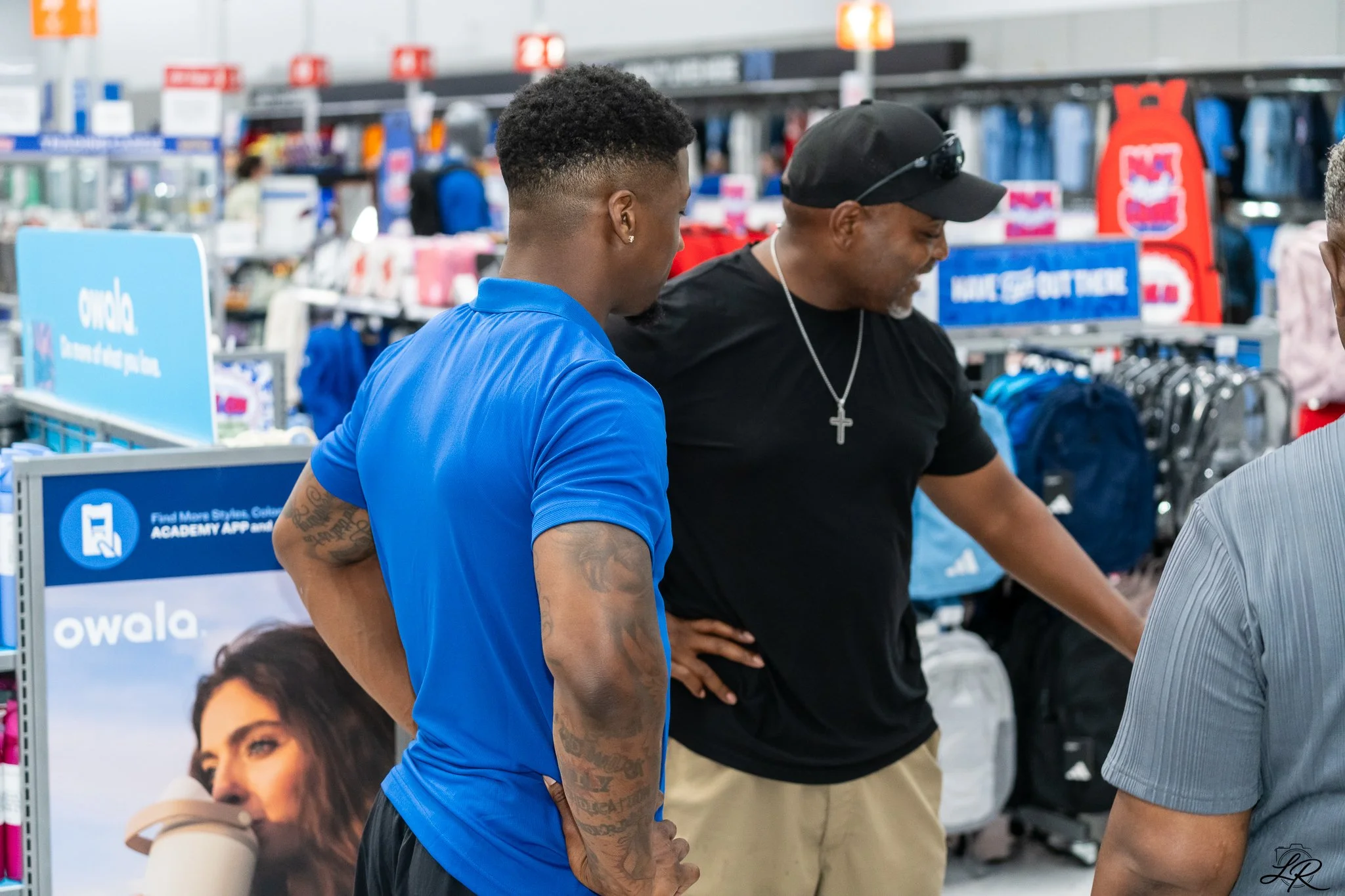 Two men browsing in an aisle of a store, with shelves stocked with various products behind them.