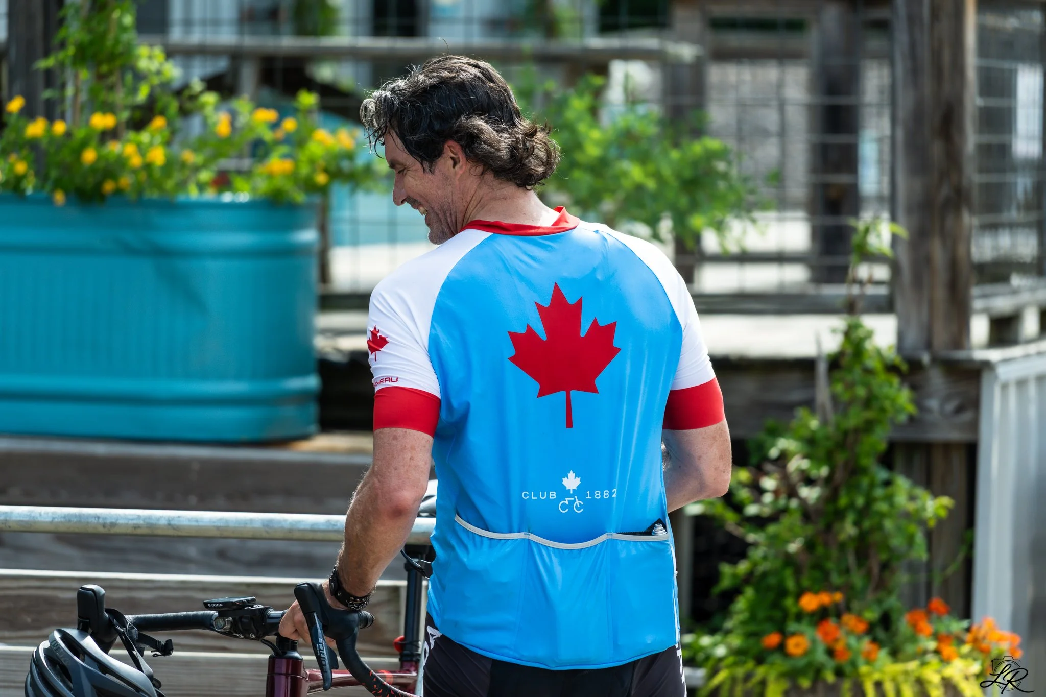 A man wearing a blue cycling jersey with a red maple leaf and white accents, standing outdoors with a bicycle.