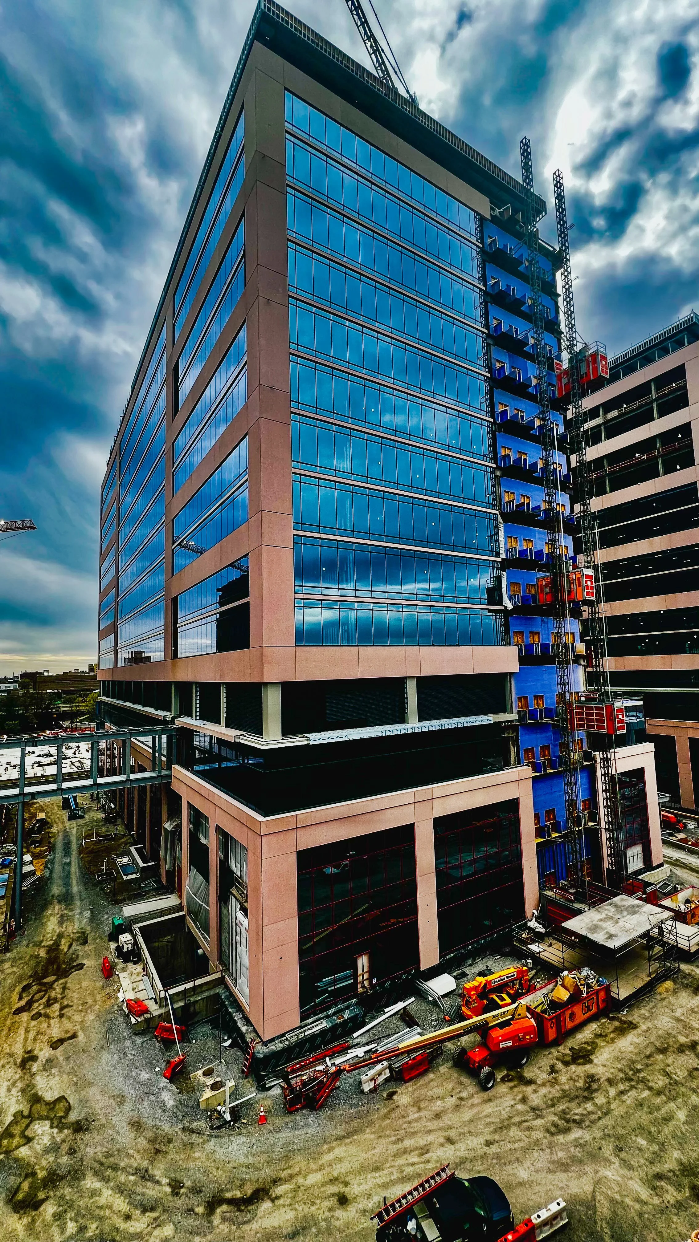 Under construction high-rise building with blue glass windows and construction equipment at the base.