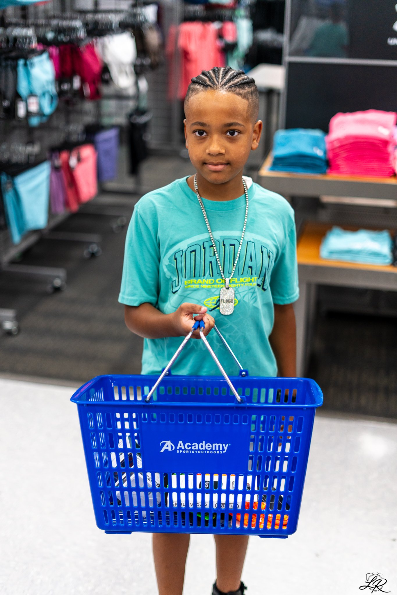 A young boy shopping at Academy Sports + Outdoors, holding an empty blue shopping basket.