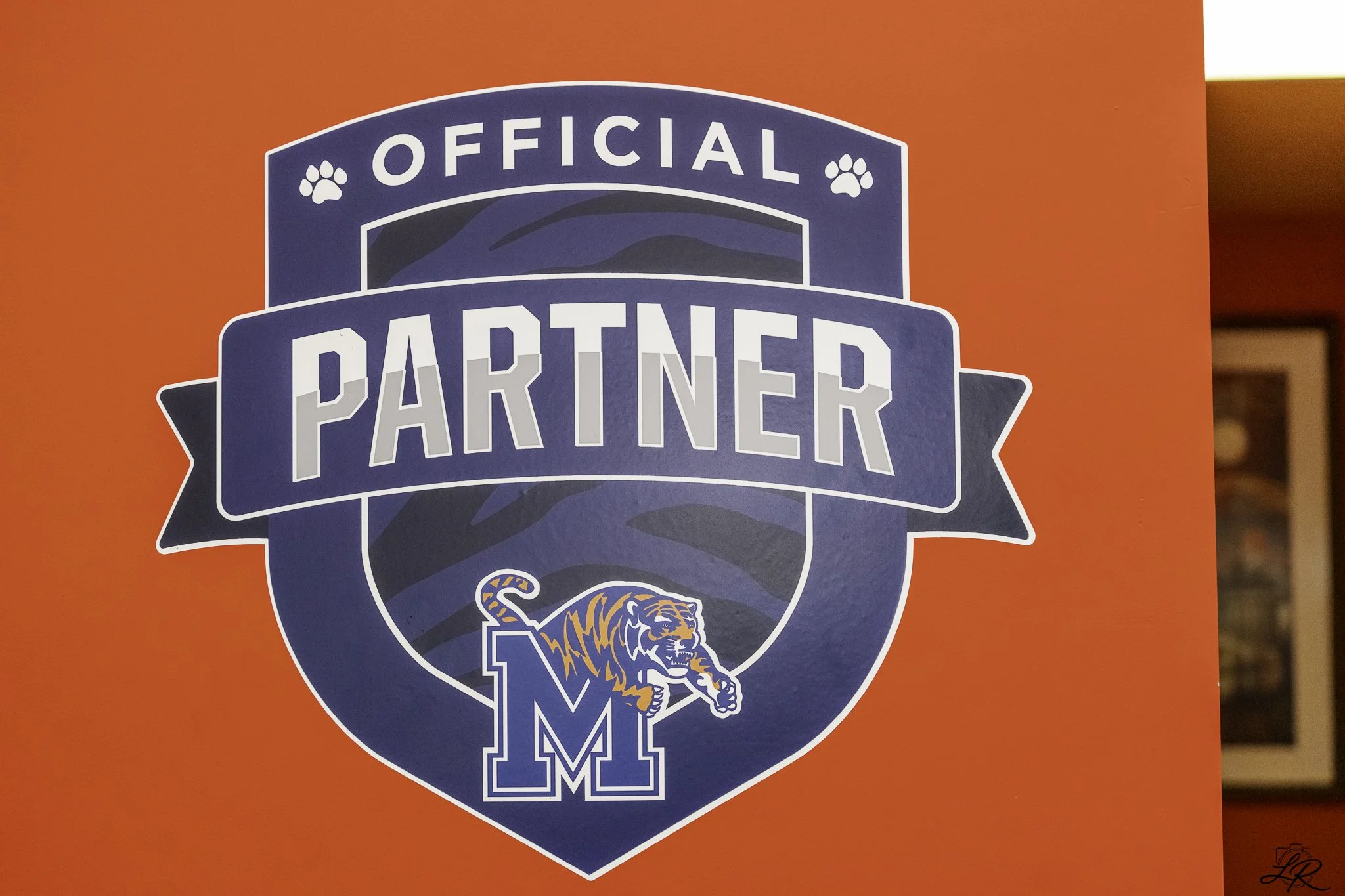 A sign with a dark blue emblem on a red background, featuring a tiger mascot and the words 'Official Partner' in white text.