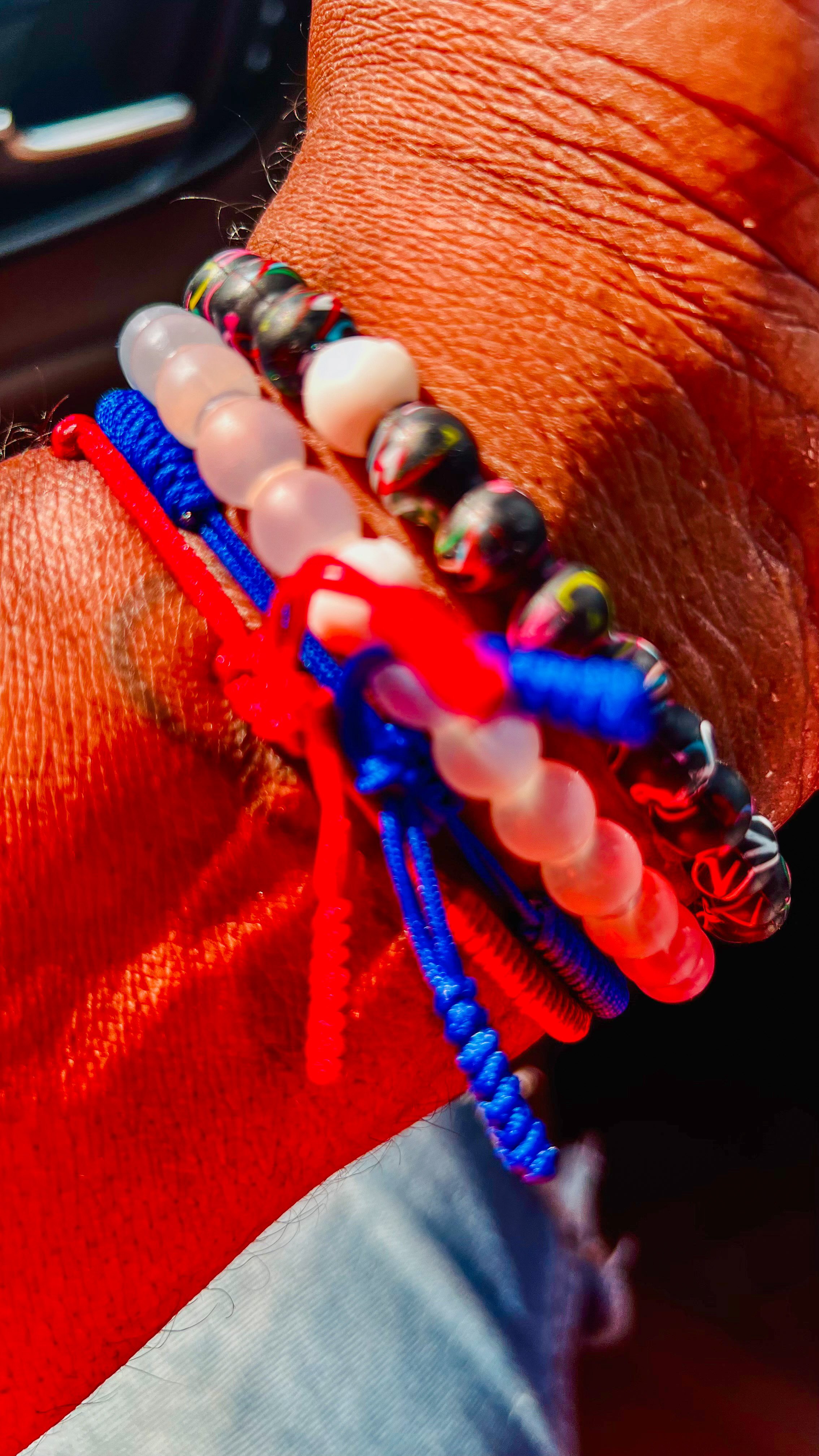 Close-up of a wrist with multiple colorful bracelets, including beaded and corded designs, on tanned skin.