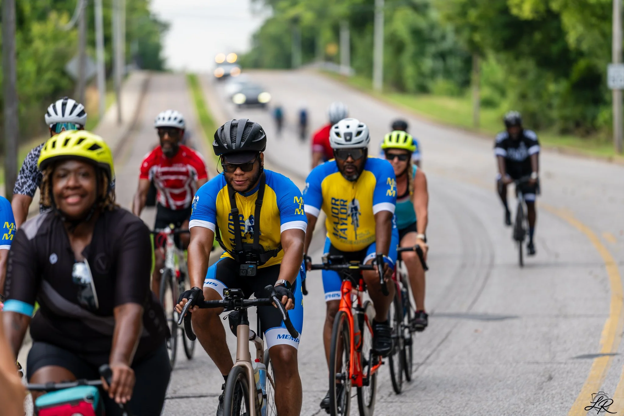 Group of cyclists riding on a road surrounded by greenery.