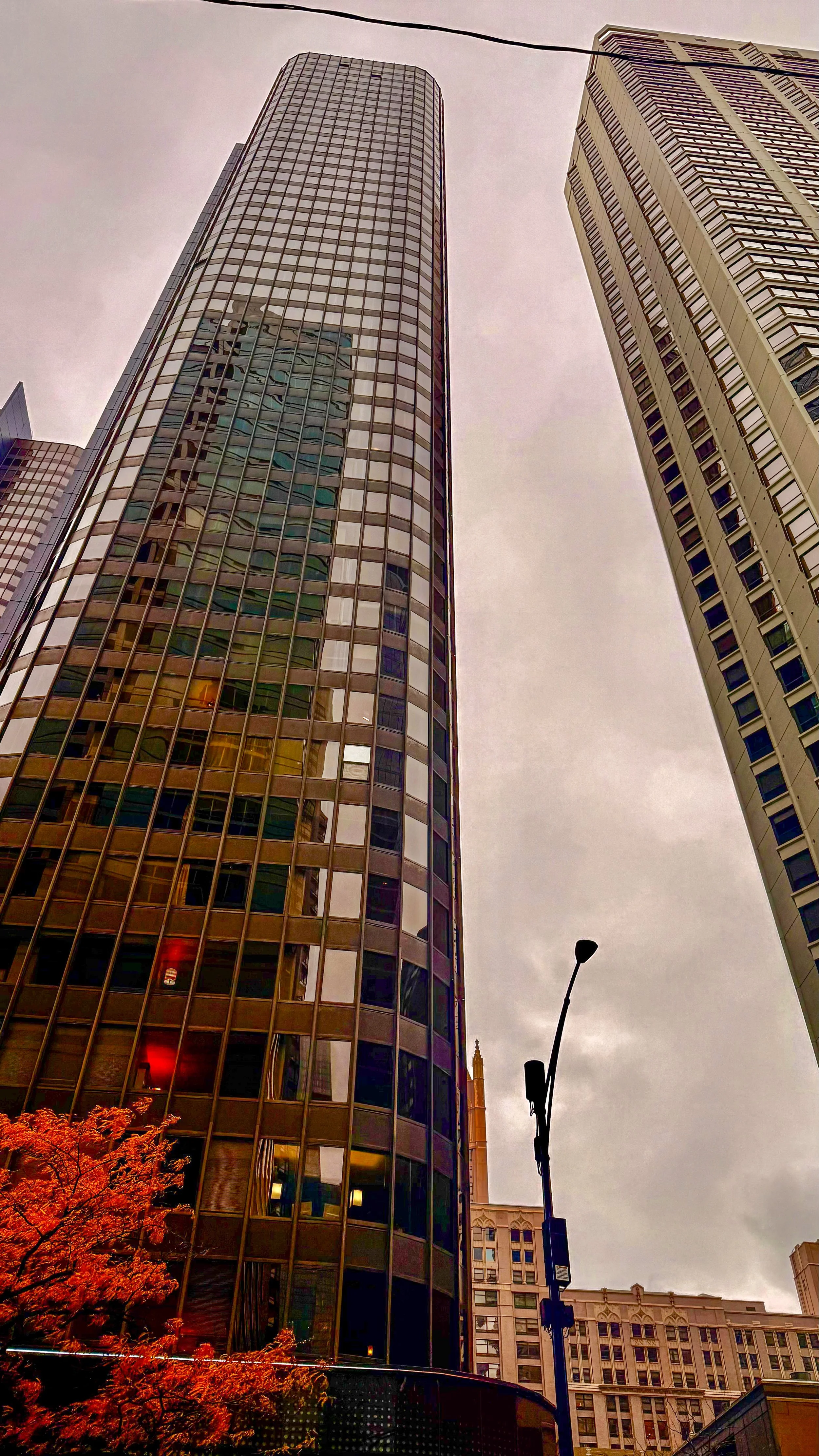 A low-angle view of tall modern skyscrapers in a city, with glass facades reflecting surrounding buildings and an overcast sky.