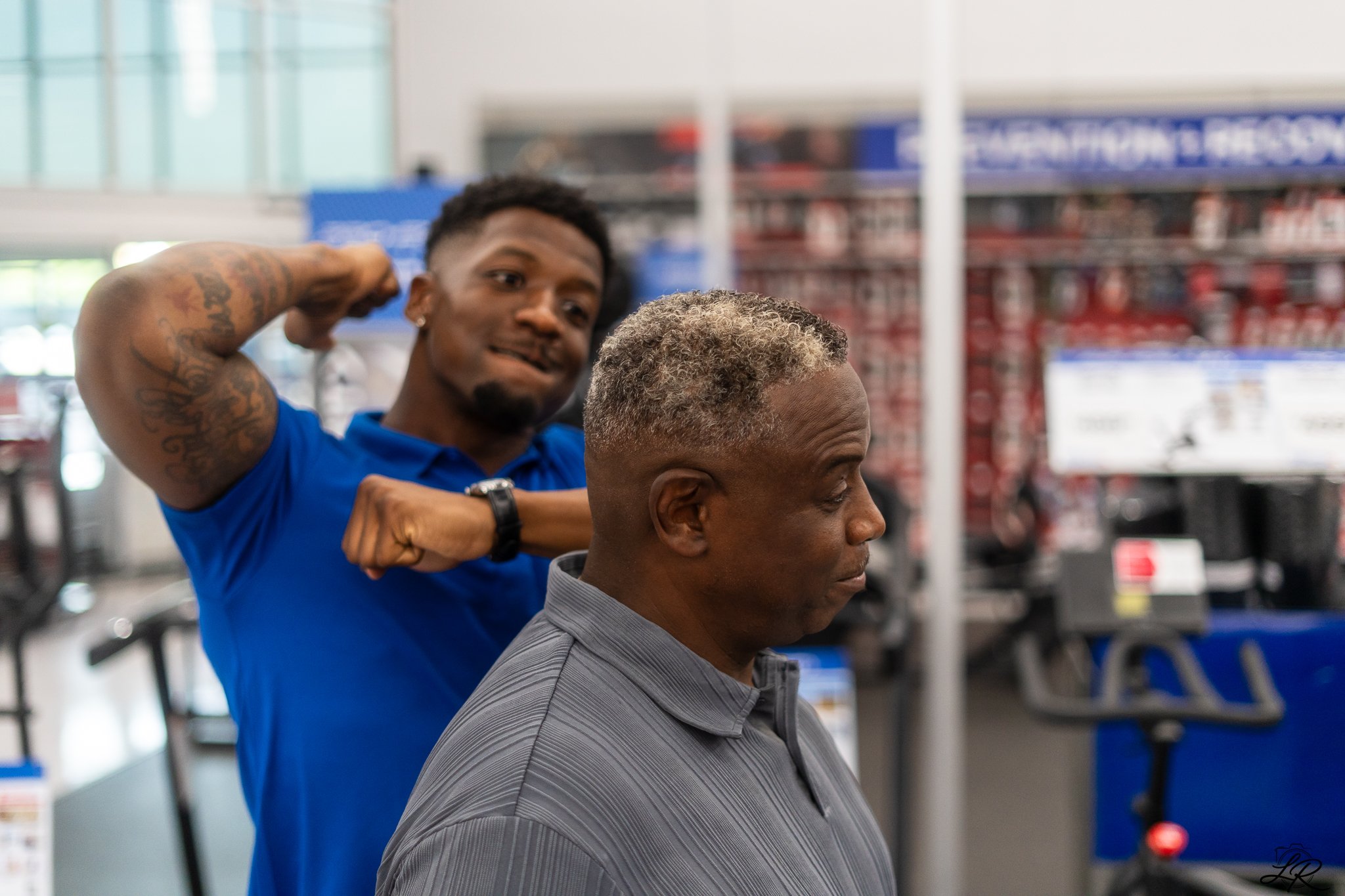 A hairstylist trims a man's hair in a store, with shelves of products in the background.