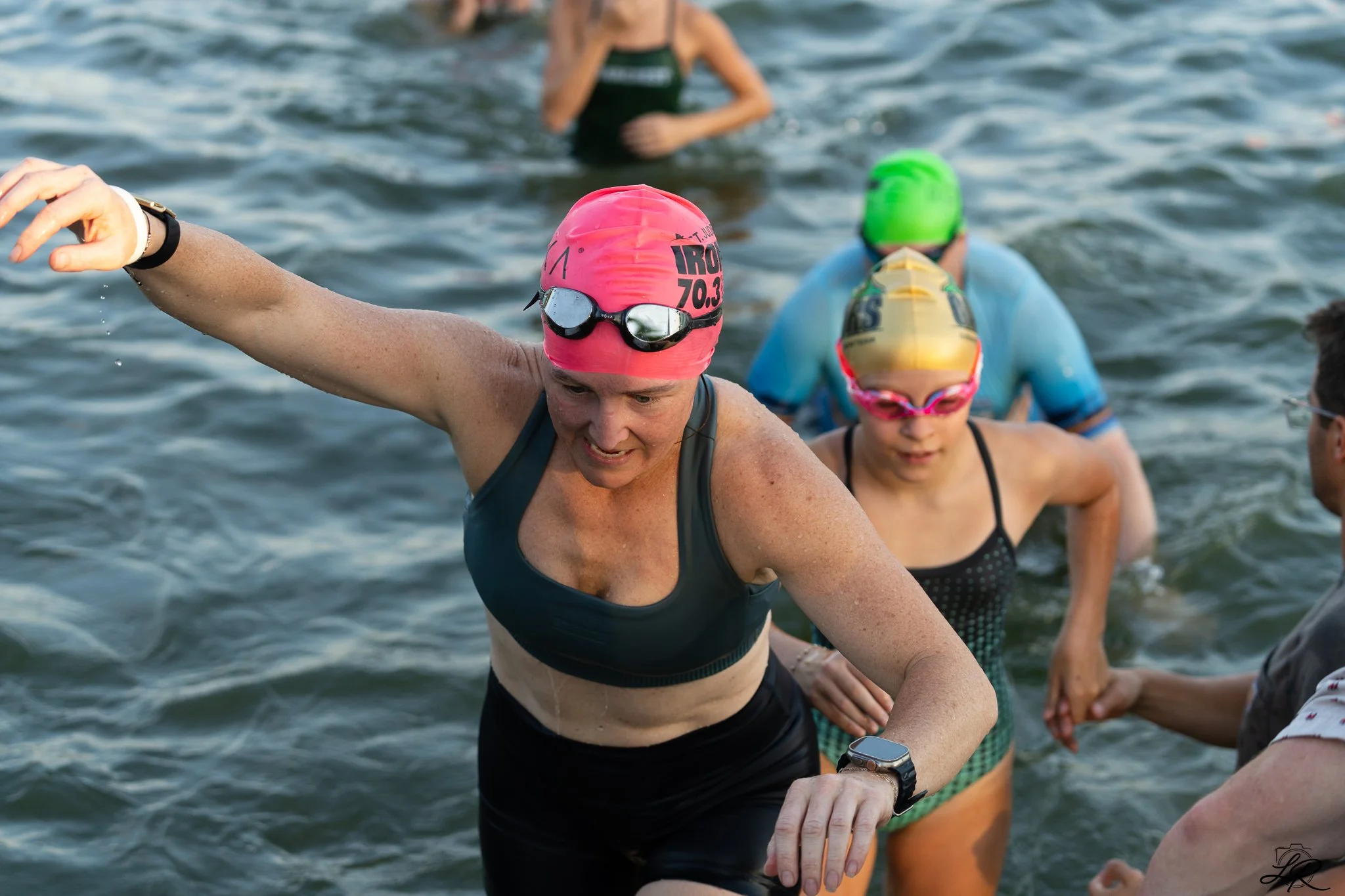 Swimmers emerging from the water after a race, wearing swim caps and goggles, with focused expressions.