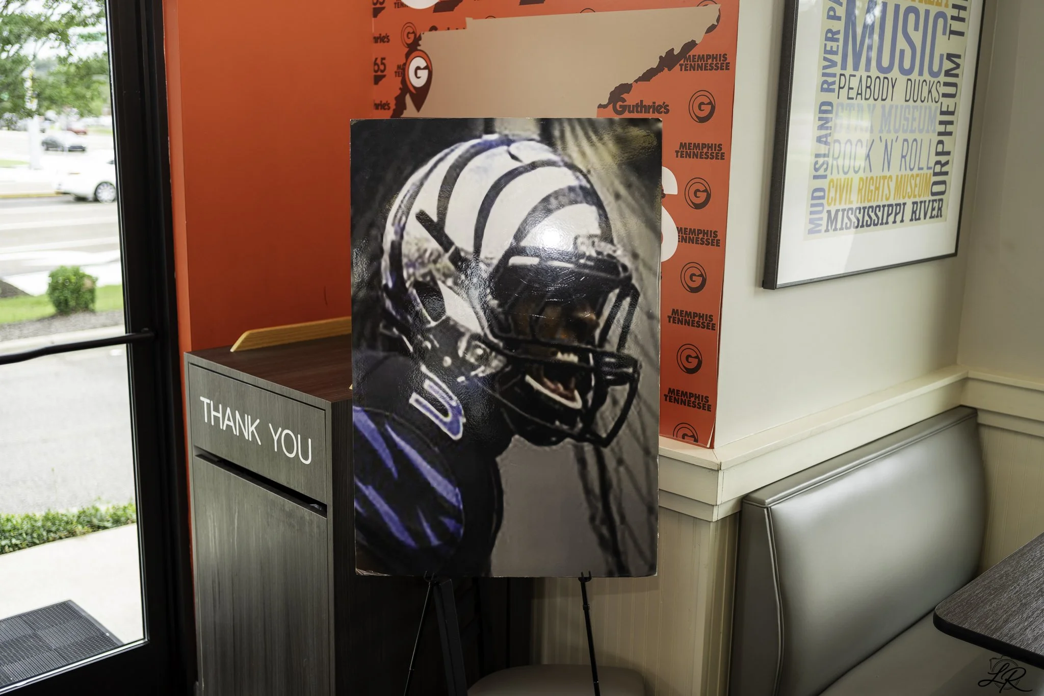 Poster of a football player in helmet and uniform inside an indoor space near a window, with a red and gray backdrop featuring map outlines and logos of Memphis Tennessee and Guthrie's.