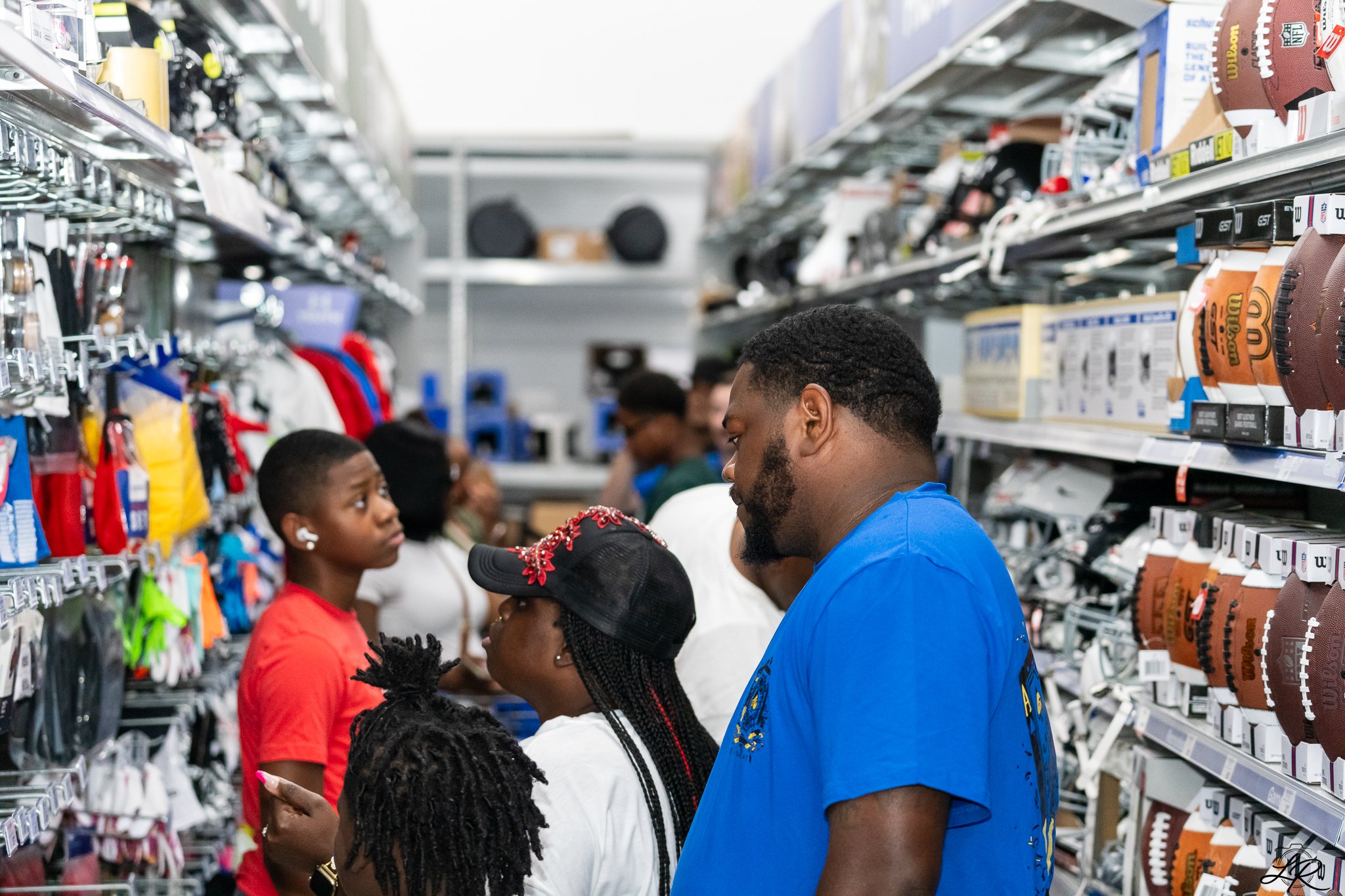 People shopping in a sporting goods store, looking at footballs on shelves.