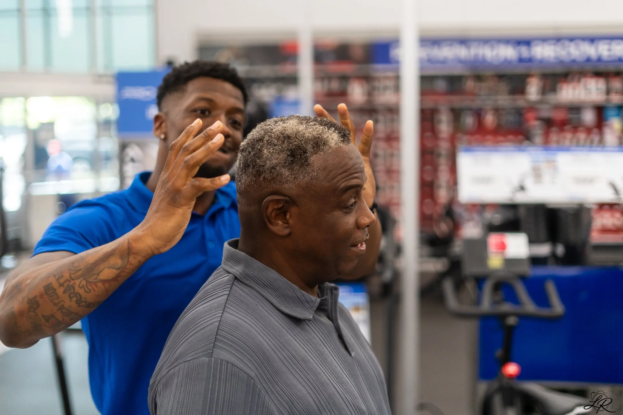 A hairstylist cutting a man's gray hair in a store aisle.