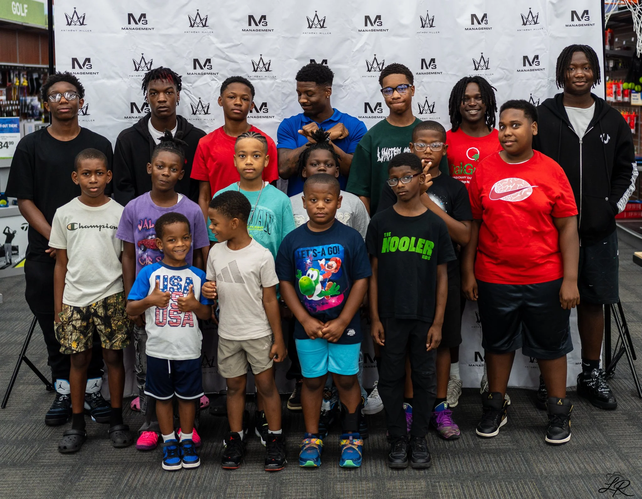 A group of boys and young men posing for a photo in front of a white backdrop with logos, standing inside a store.
