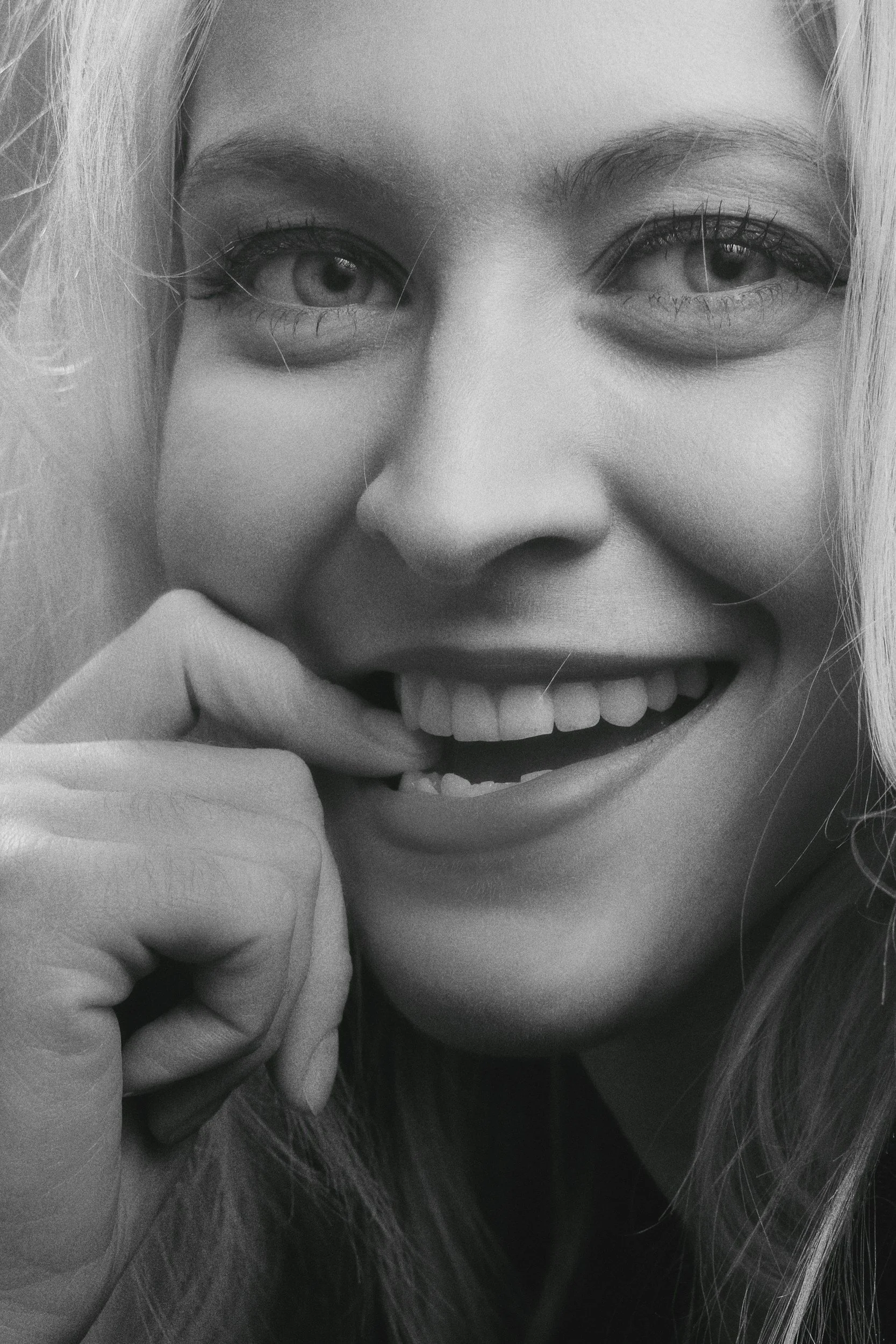 A close-up black and white photo of a woman smiling and holding her chin with her hand.