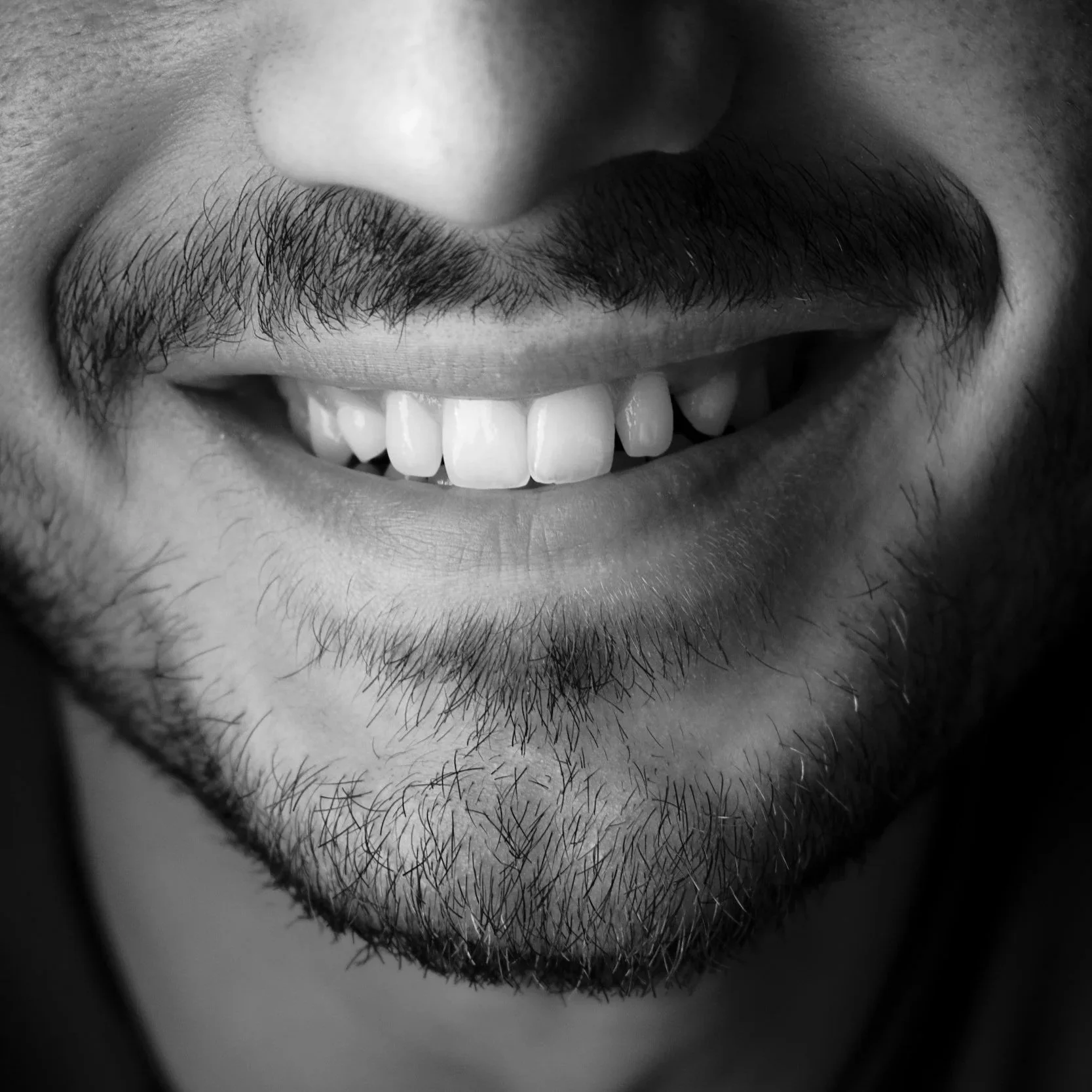 Close-up of a smiling man's mouth with facial hair in black and white.