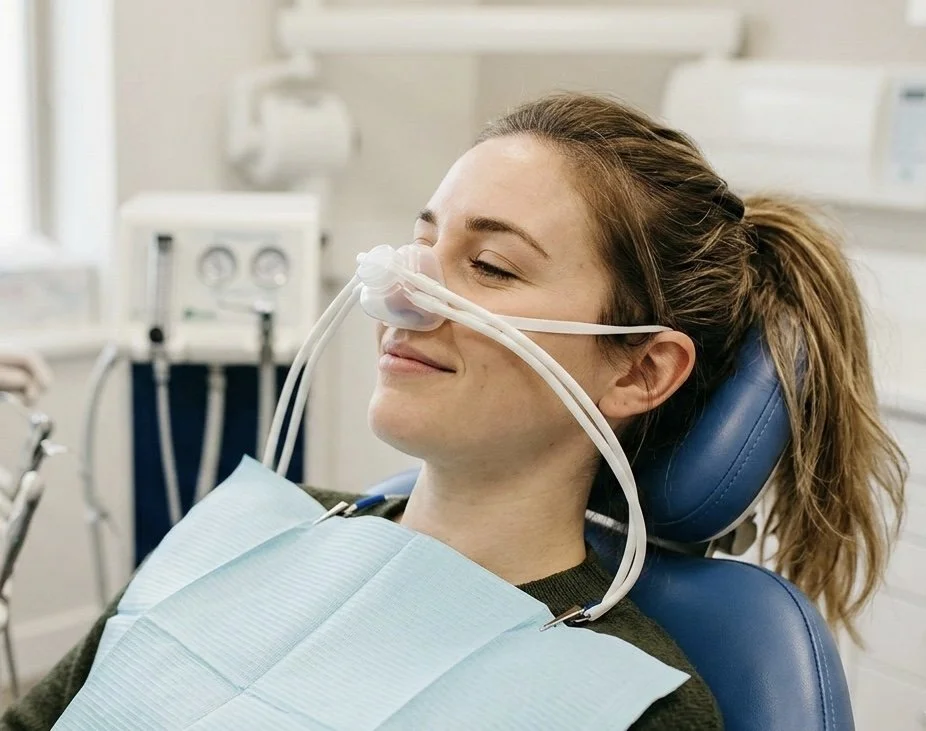 Woman in a dental chair with nasal oxygen tube, smiling with eyes closed in a dental clinic.