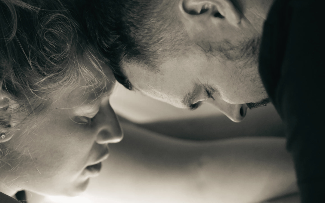 Close-up of a man and woman with their foreheads touching, eyes closed, in black and white.