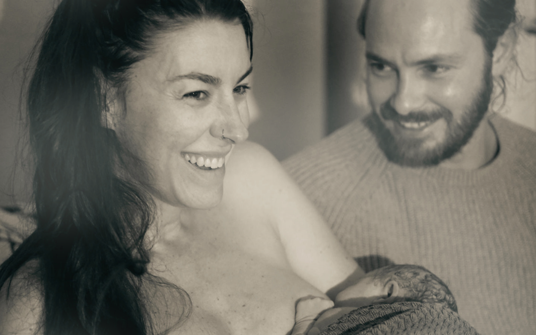 A woman breastfeeding her baby, with a man smiling beside her, in a candid, intimate moment.