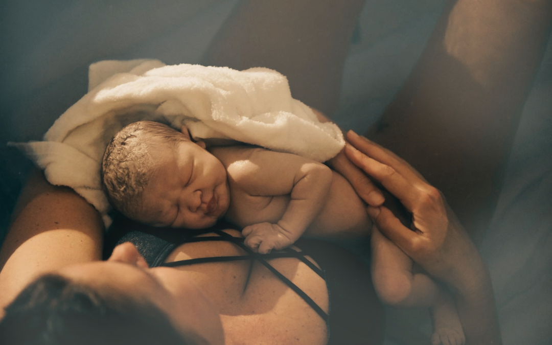 A newborn baby sleeping on moms chest in a birthing pool, wrapped in a white towel.