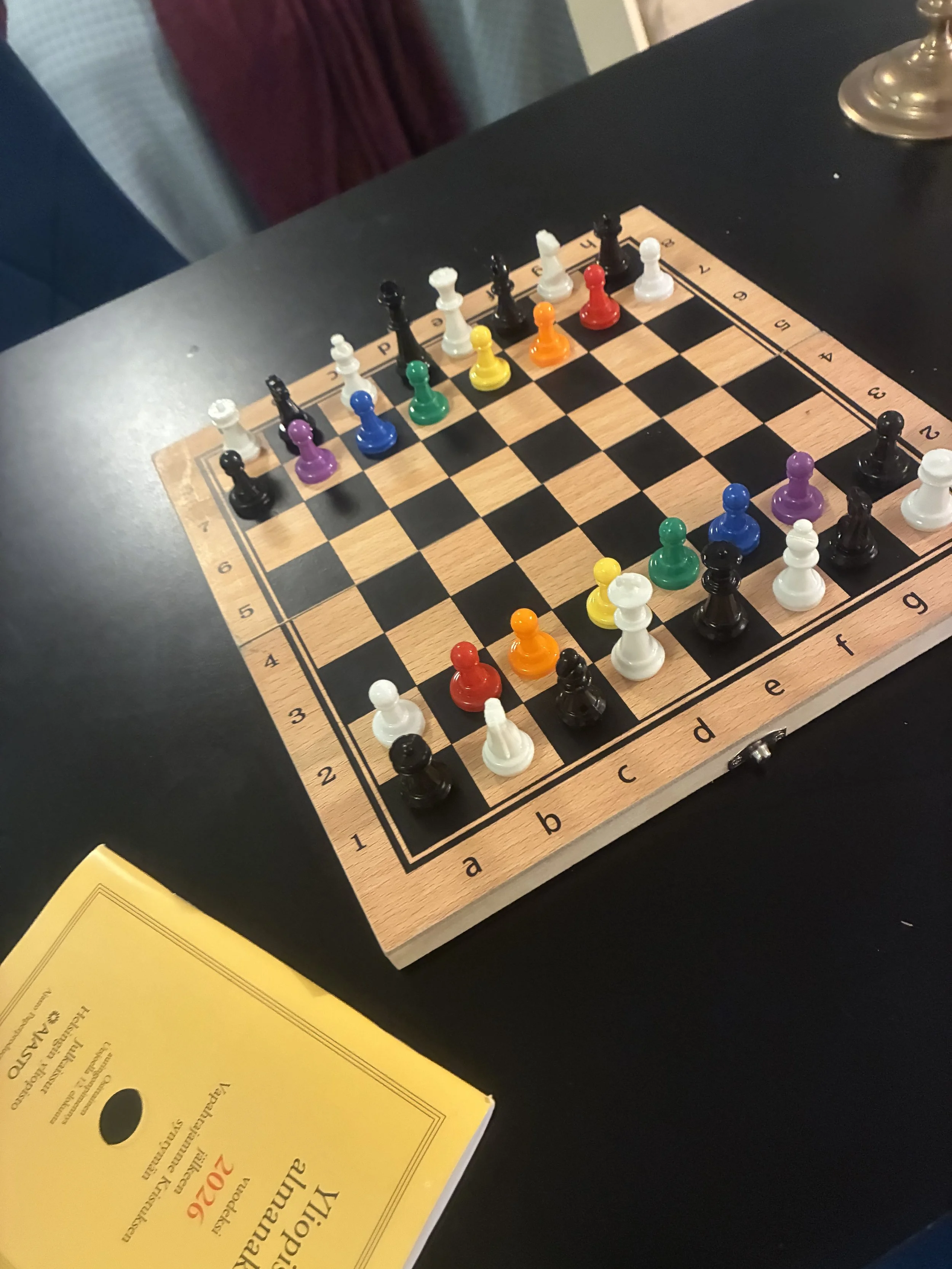 A chessboard set up for a game with colorful pieces on a black table.