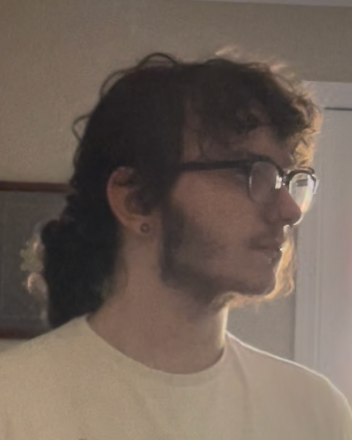 A side profile photo of a woman with light facial hair, glasses, and hair pulled back. She is illuminated by the sun coming through an out-of-view window.