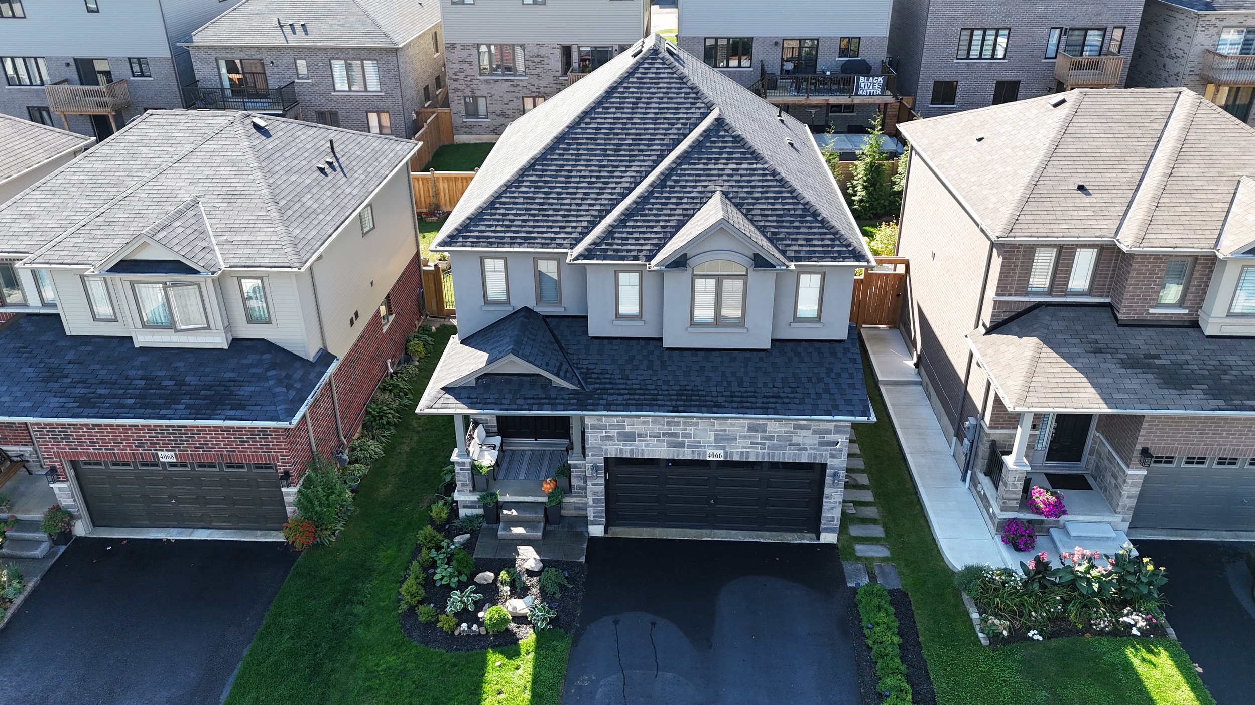An aerial view of a suburban neighborhood showing three houses with landscaped yards and paved driveways.