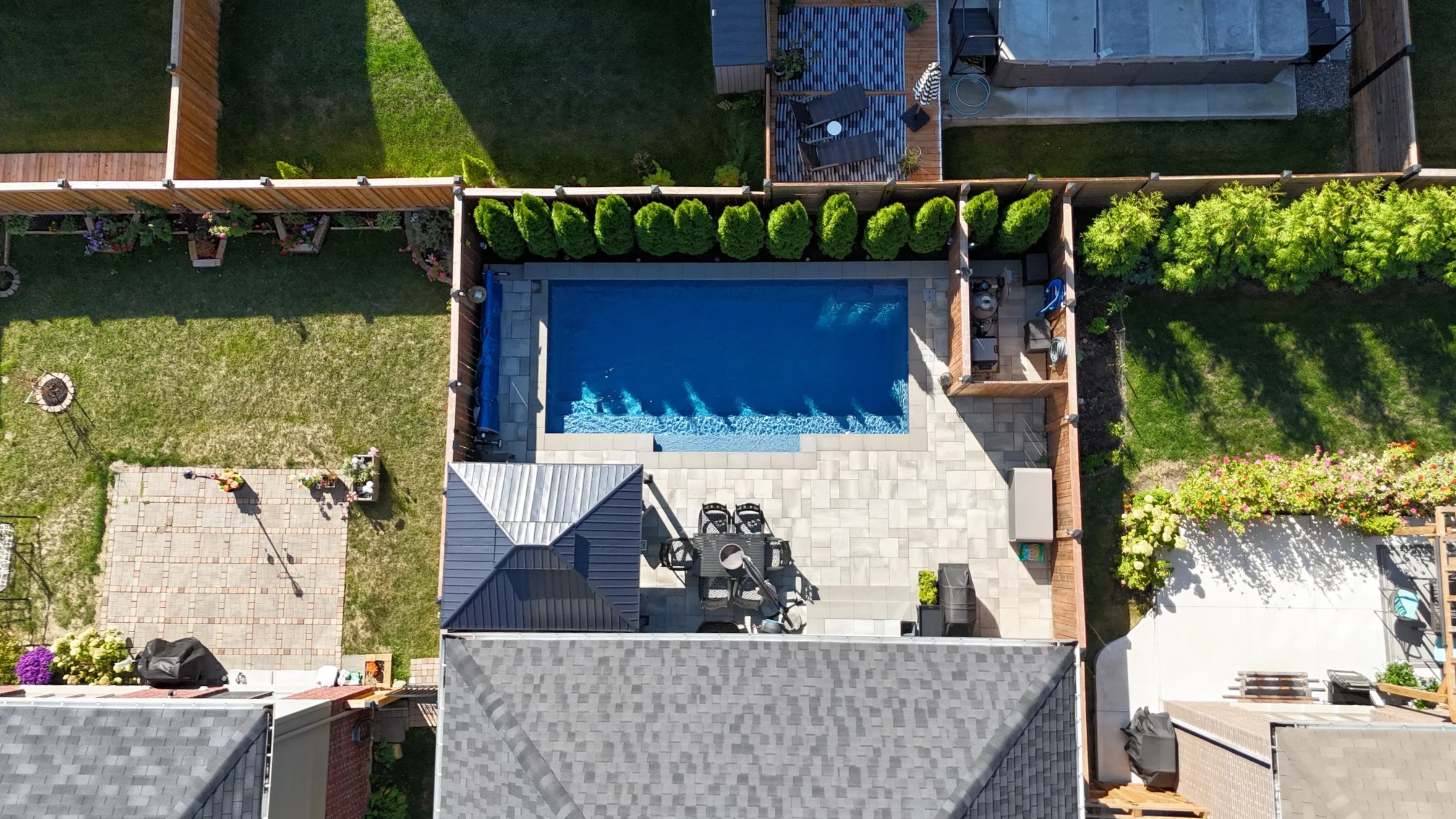 Real Estate Niagara Homes - Aerial view of a backyard pool area with surrounding patio, greenery, and outdoor furniture.