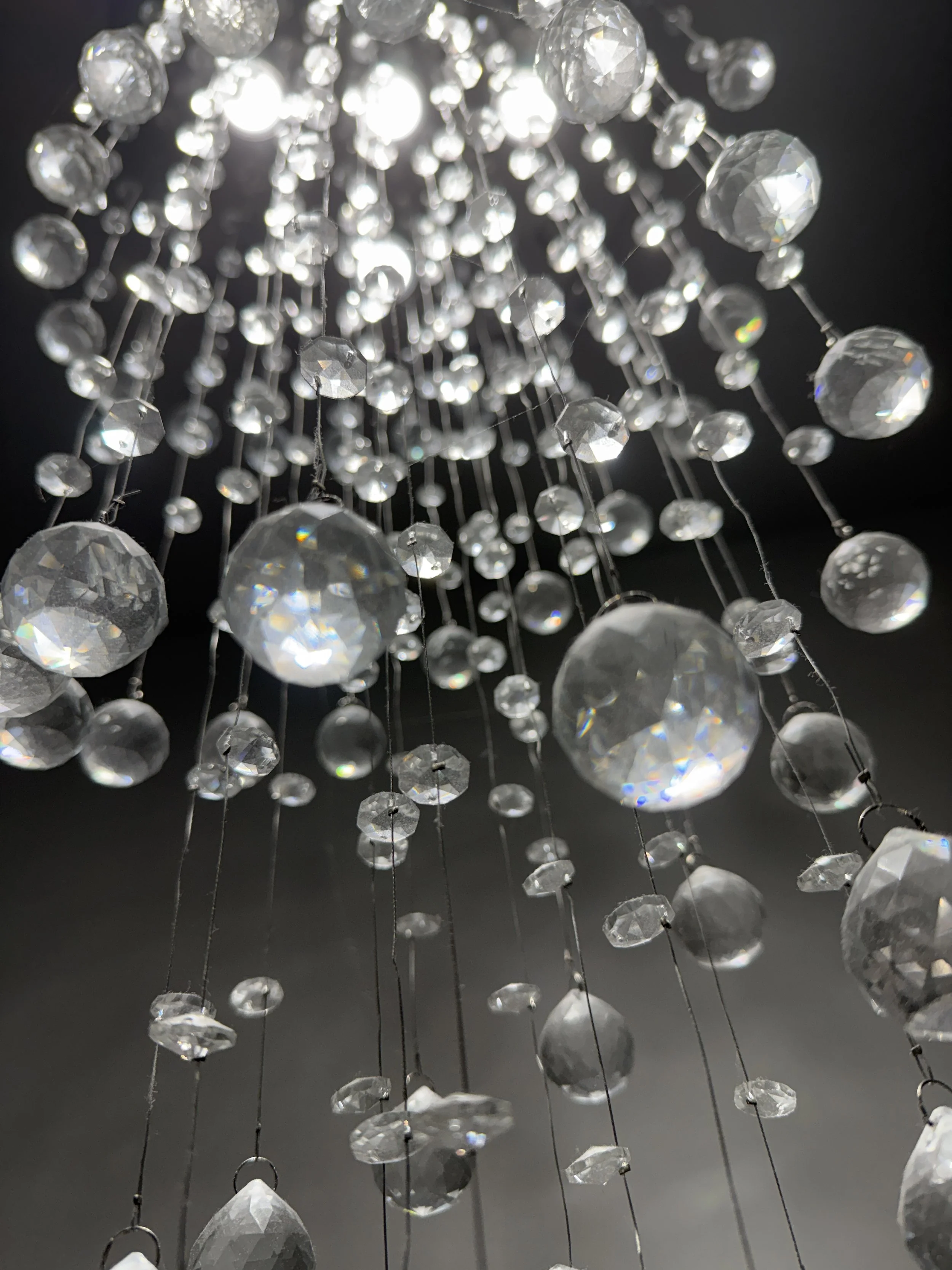 Real Estate Niagara Homes - Close-up of a crystal chandelier with light reflected through the faceted crystals, hanging against a dark background.