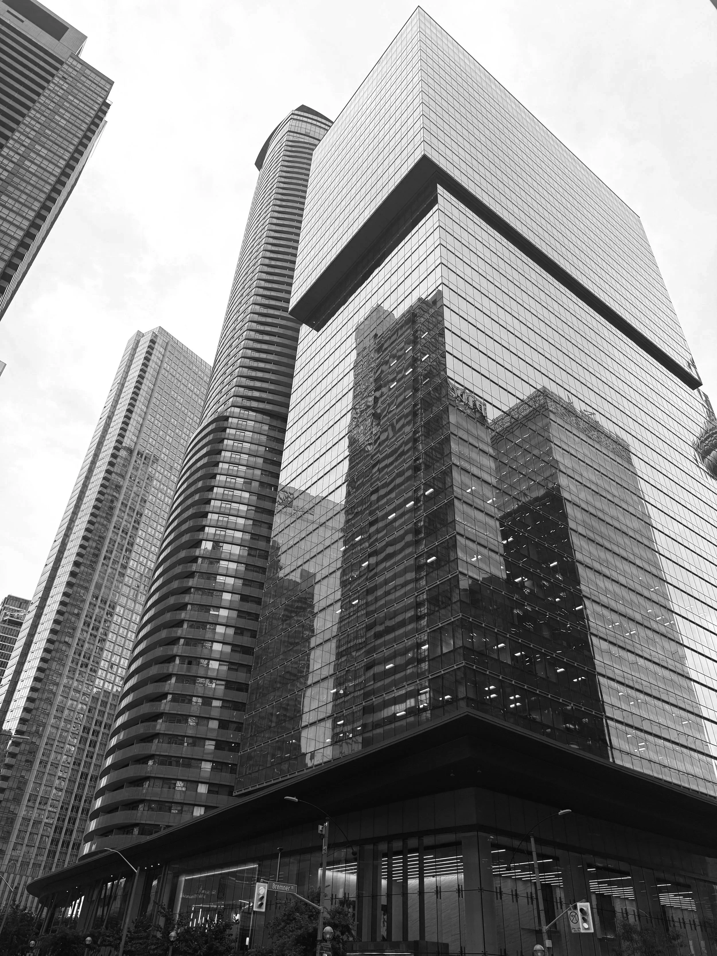 Black and white photo of modern skyscrapers with glass facades reflecting each other, taken from street level.