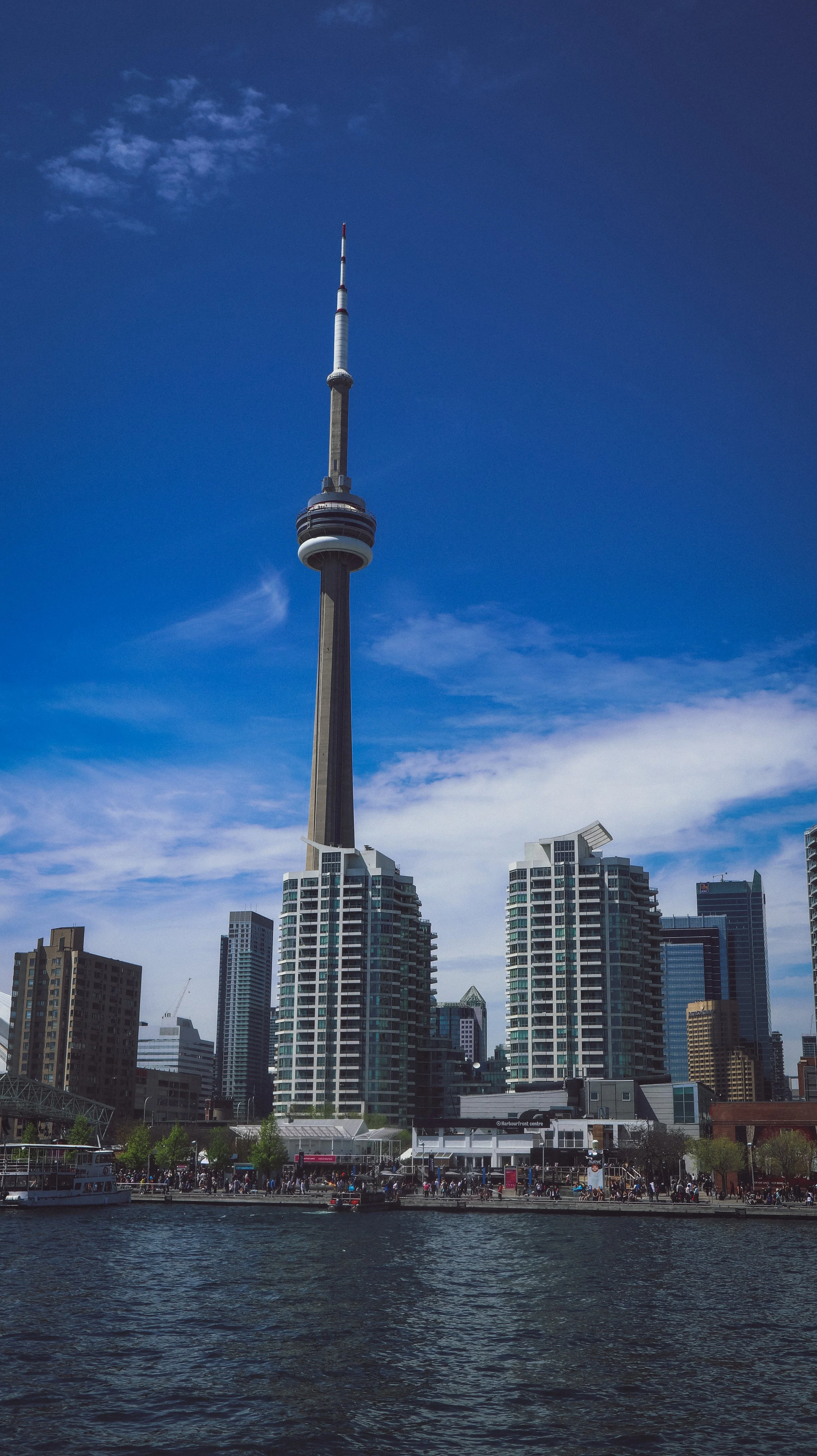 Skyline of Toronto with CN Tower and surrounding buildings along a waterfront with boats.