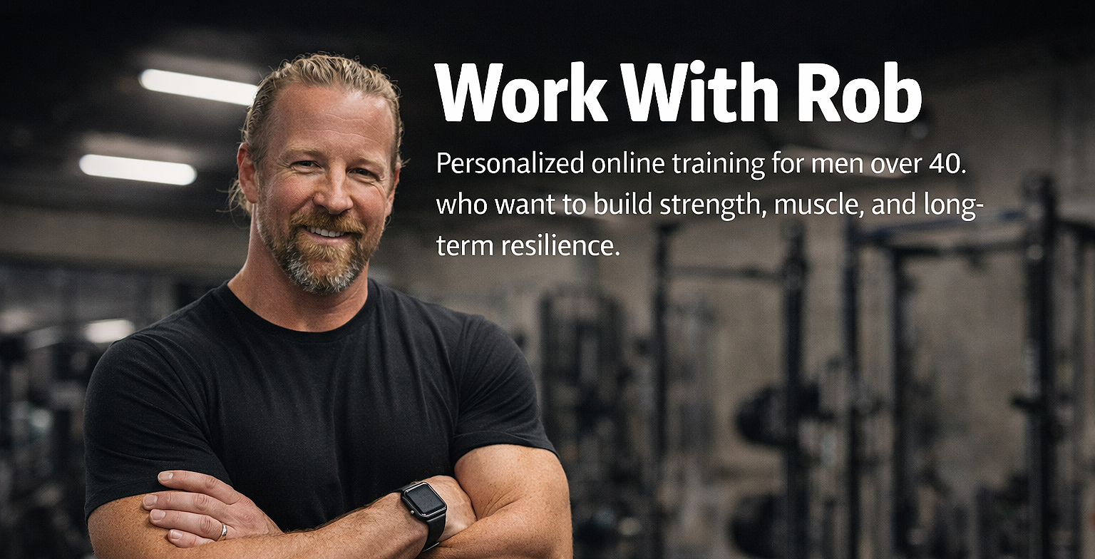 Rob, the personal trainer behind Iron After 40 stands smilling, wearing a black t-shirt and smartwatch, in a gym with weight racks in the background.