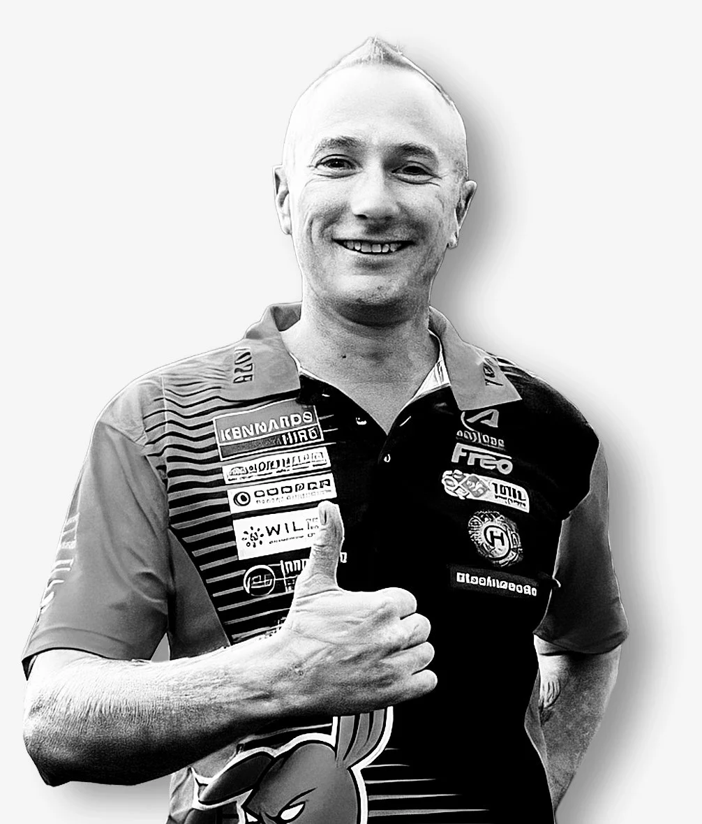 A smiling man with a mohawk hairstyle giving a thumbs-up, wearing a sports jersey with sponsor logos.