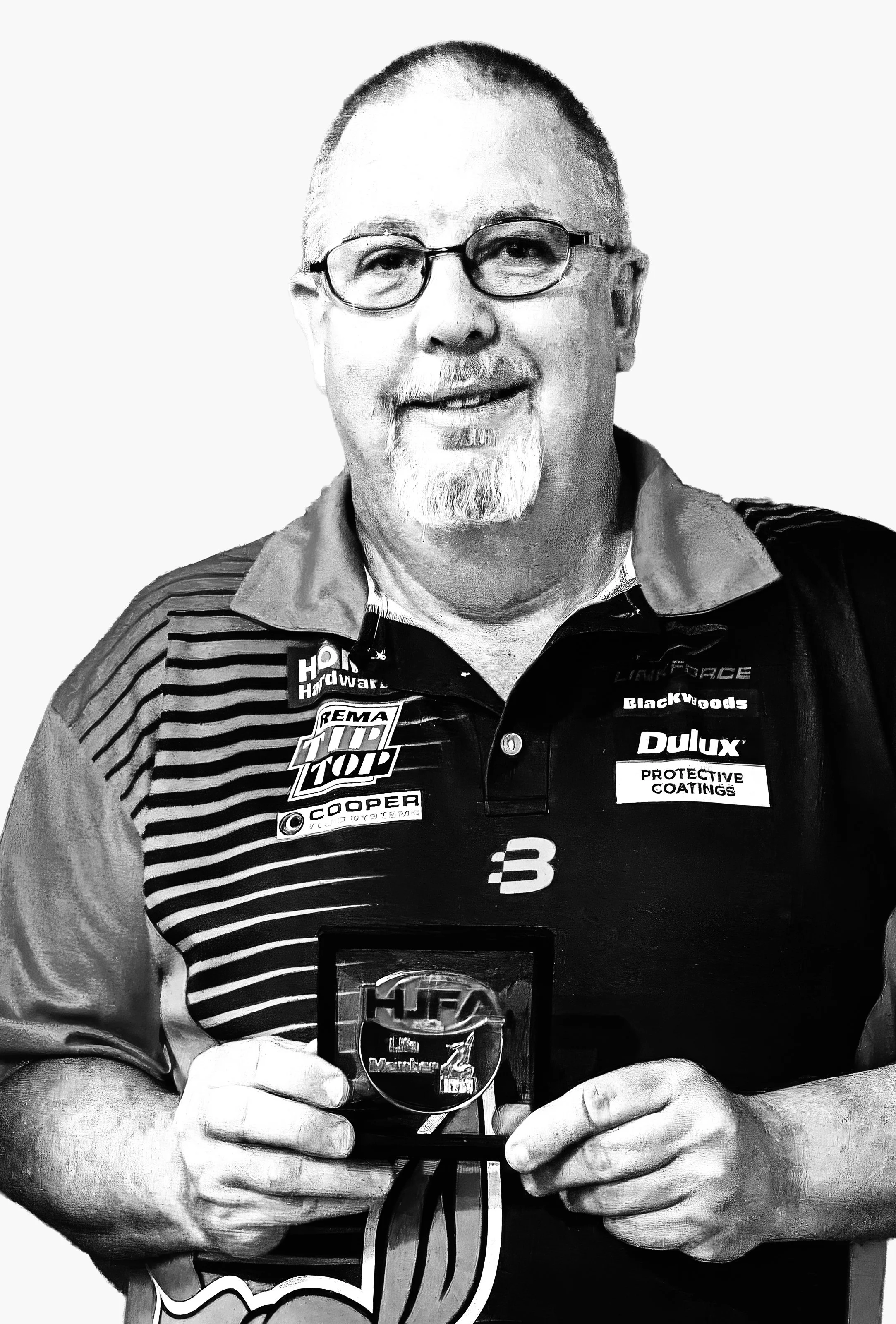 A man with glasses and a goatee holding a trophy, wearing a racing team shirt with various brand logos.
