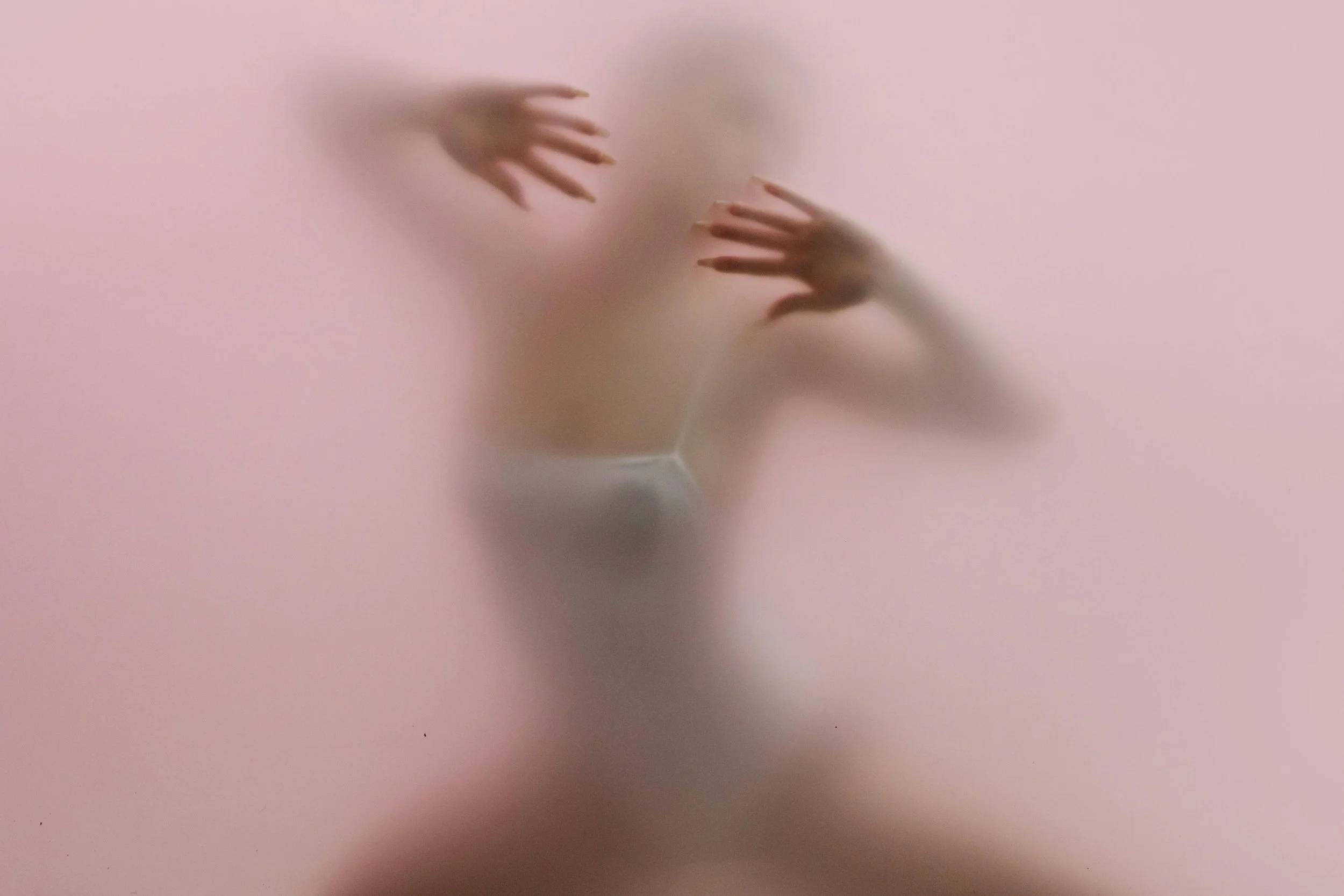 Person pressing their hands and face against a translucent pink surface, creating a blurry, abstract appearance.