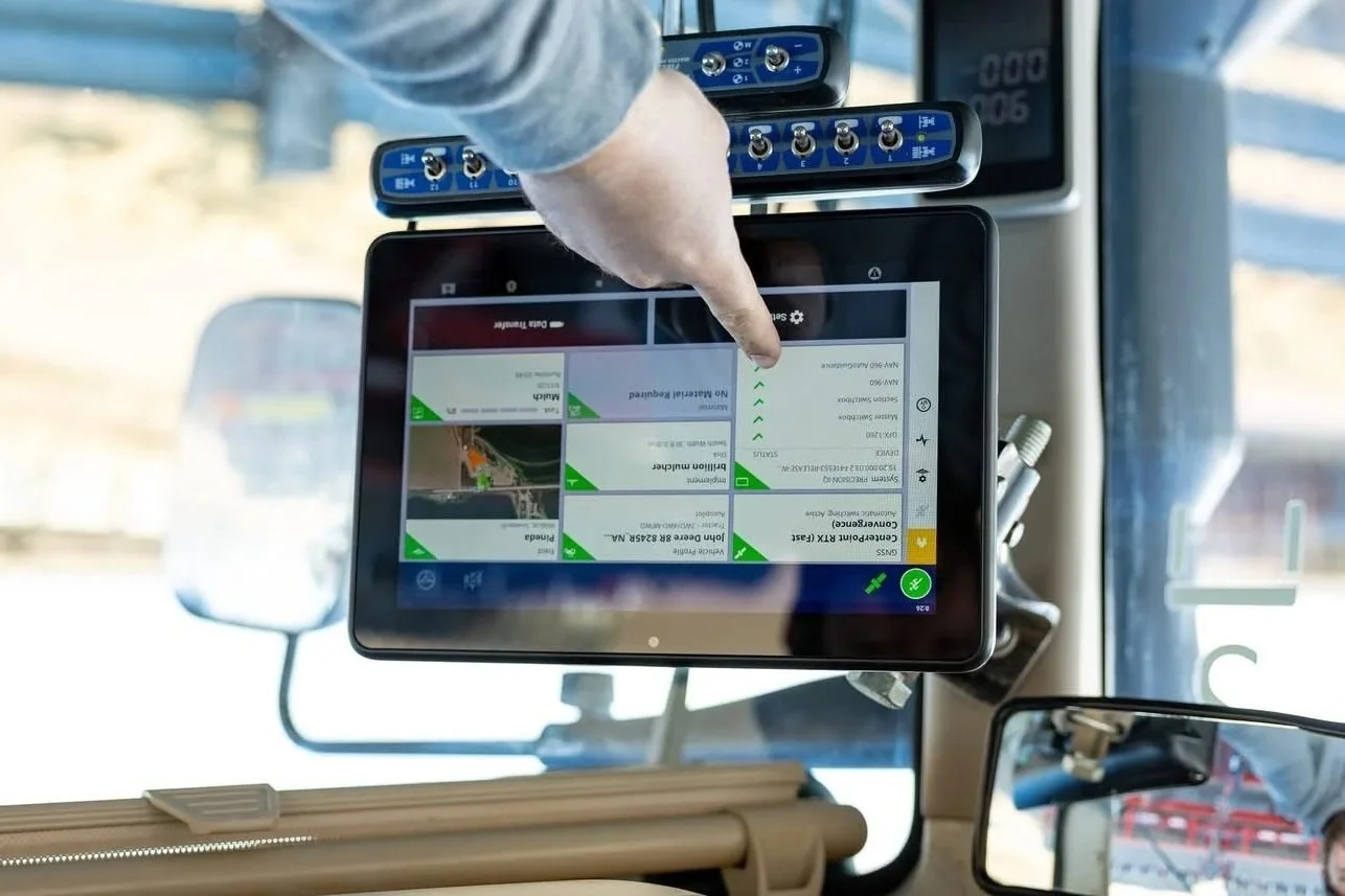 A person's hand interacting with a digital tablet mounted inside a vehicle, with a background showing side mirrors and a sunny outdoor scene.
