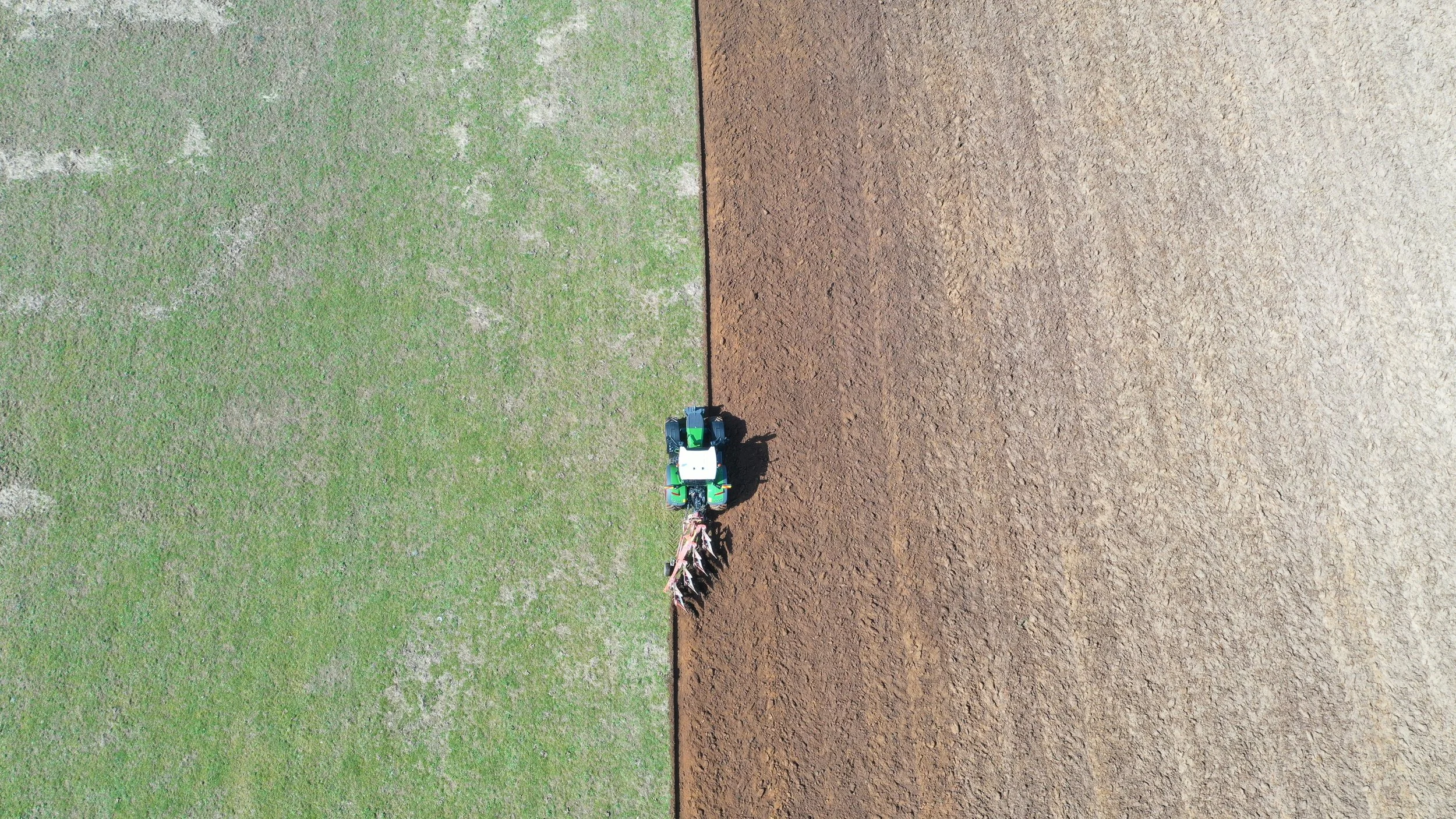 A drone flying over divided land with grass on the left and brown dirt on the right.