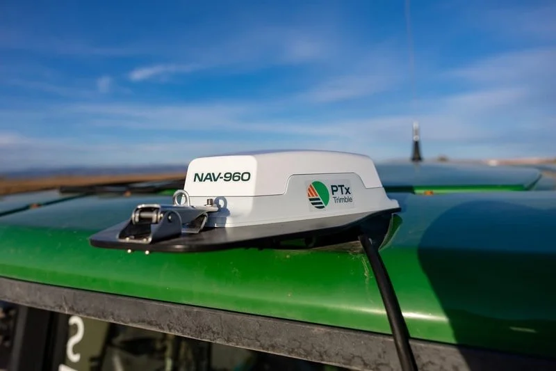 A close-up of a green drone with a white GPS device labeled 'NAV-960' and 'PTx Trimble' mounted on top, outdoors with a clear blue sky and horizon in the background.