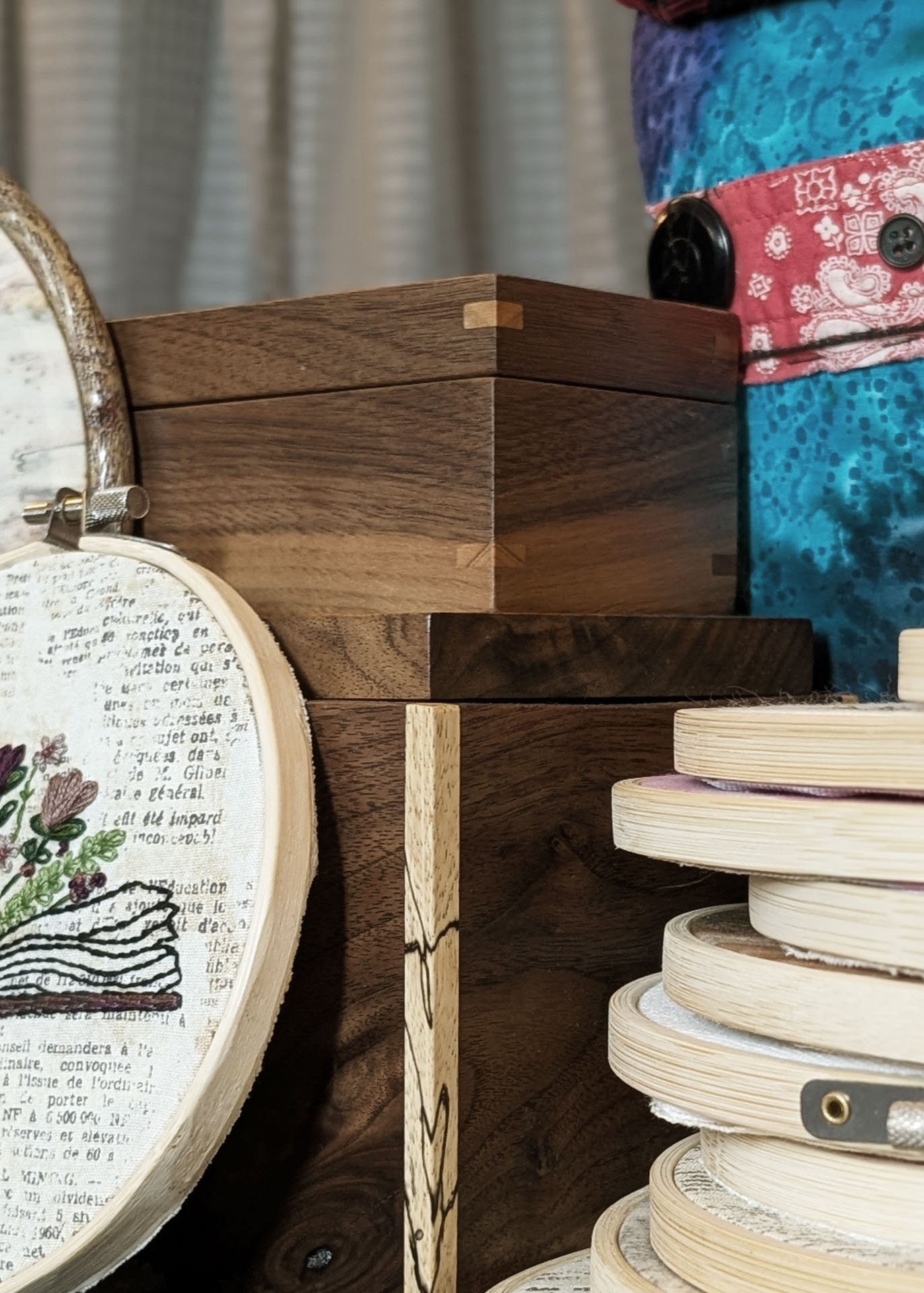 Close-up of wooden embroidery hoops and wooden boxes, with colorful fabric in the background.
