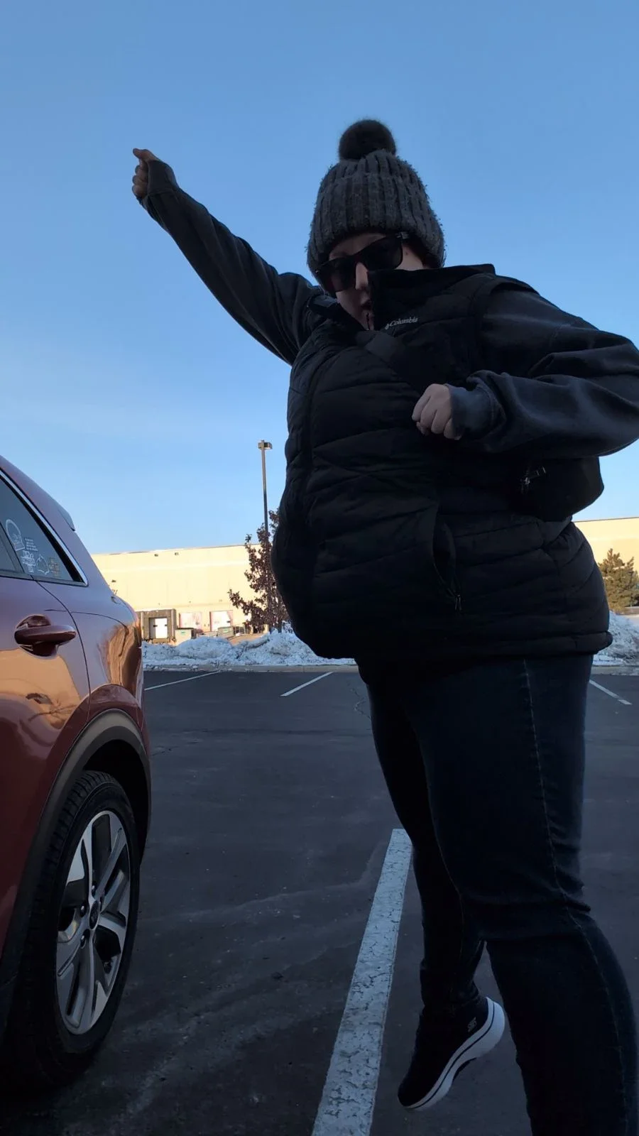 Person mid-jump with leg extended in a parking lot wearing a winter hat and jacket