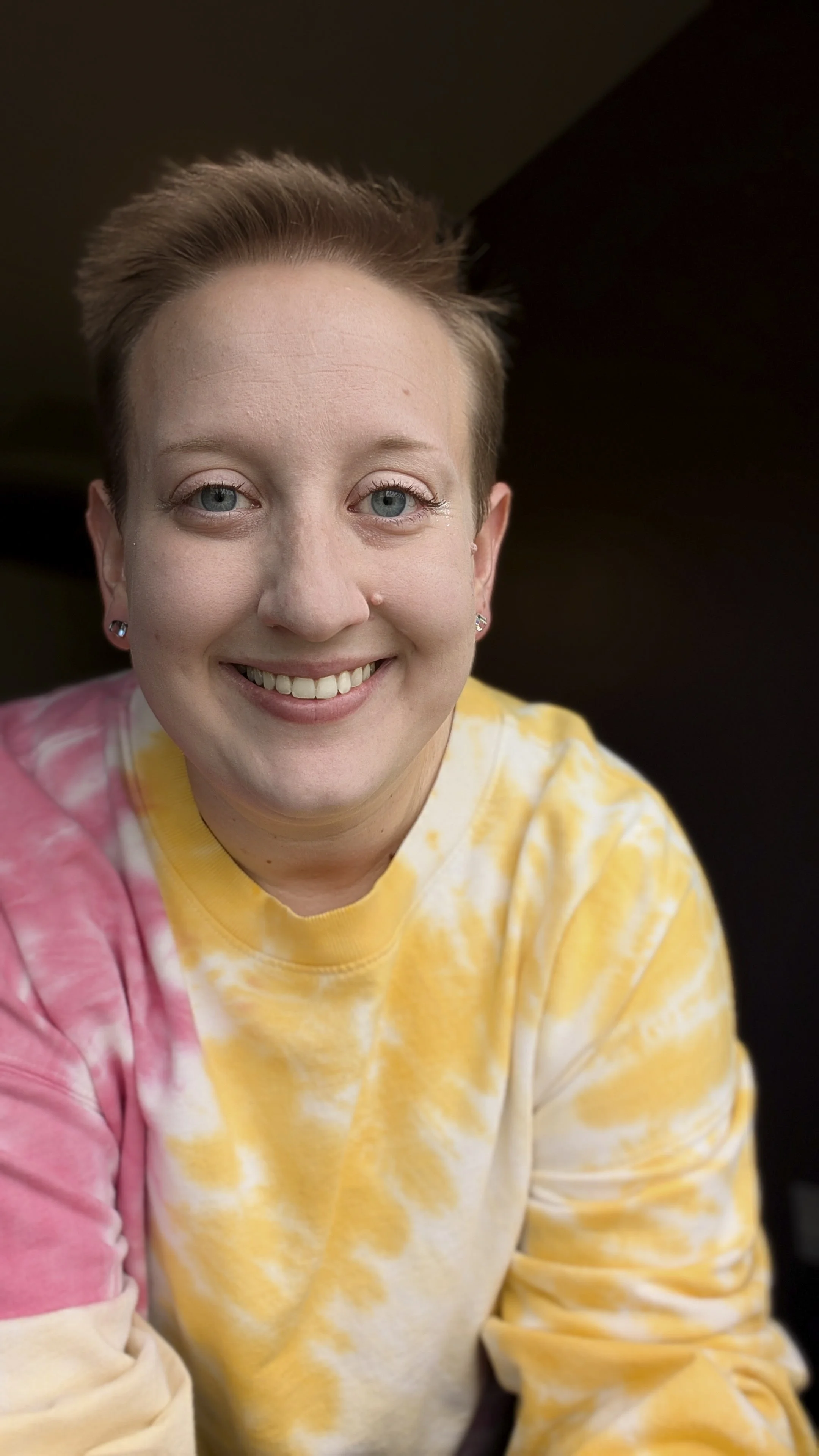 Portrait of the Chaptered Goods founder and maker smiling in a pink and yellow tie-dye sweatshirt.