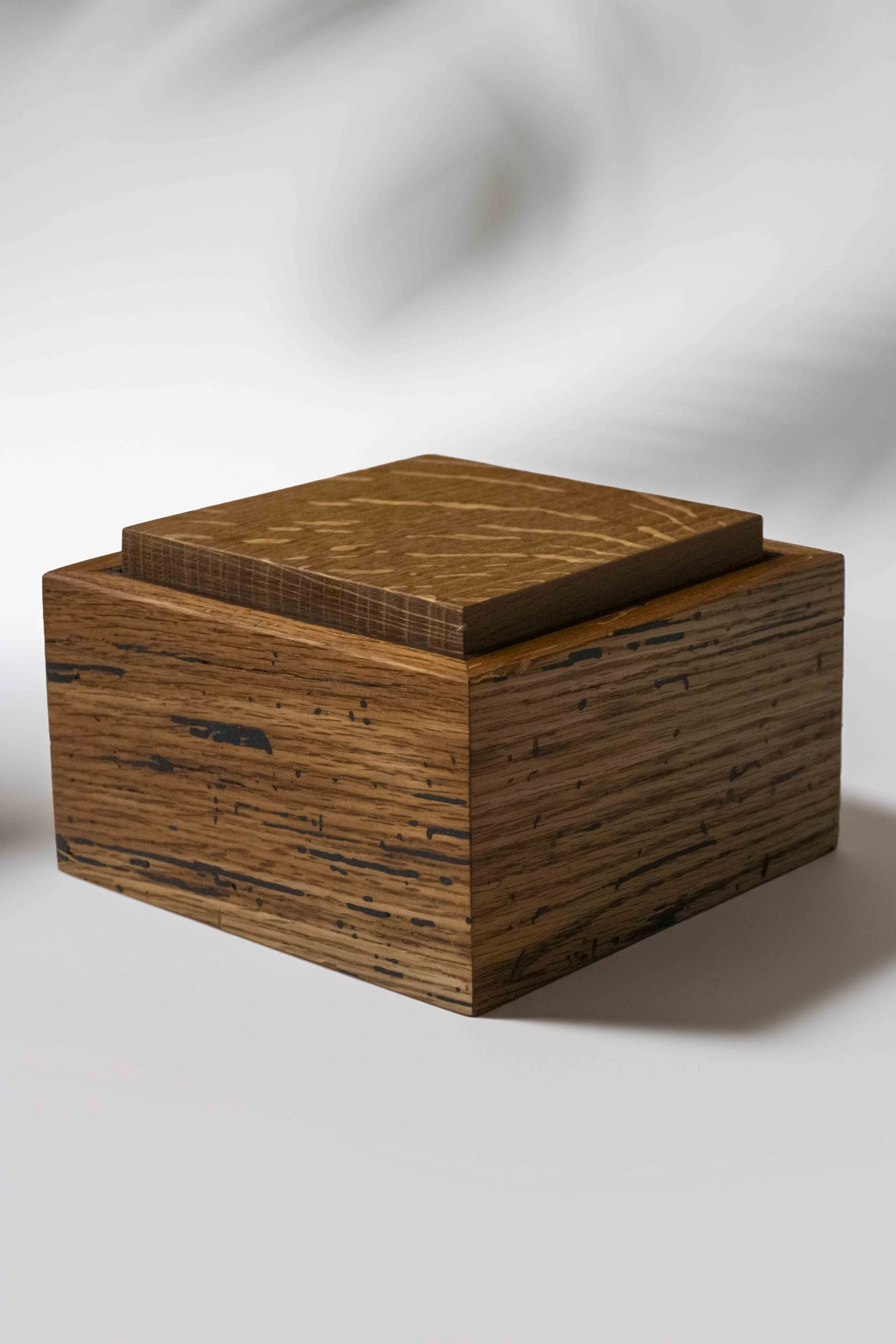 Close-up of a wooden cube with a smaller wooden panel on top, set against a gray background.