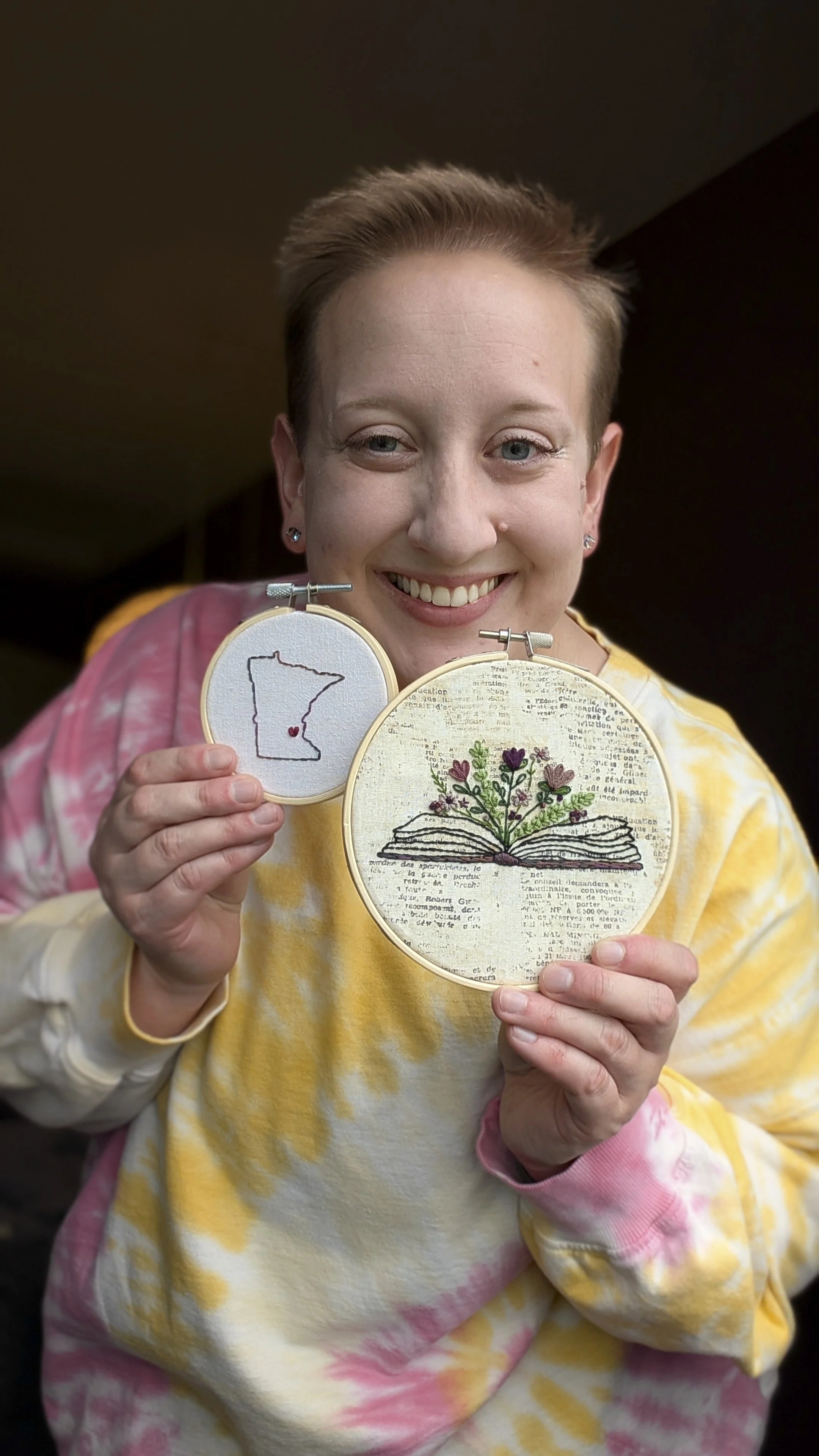 Chaptered Goods founder holding handmade embroidered hoop art featuring a Minnesota design and floral book motif.