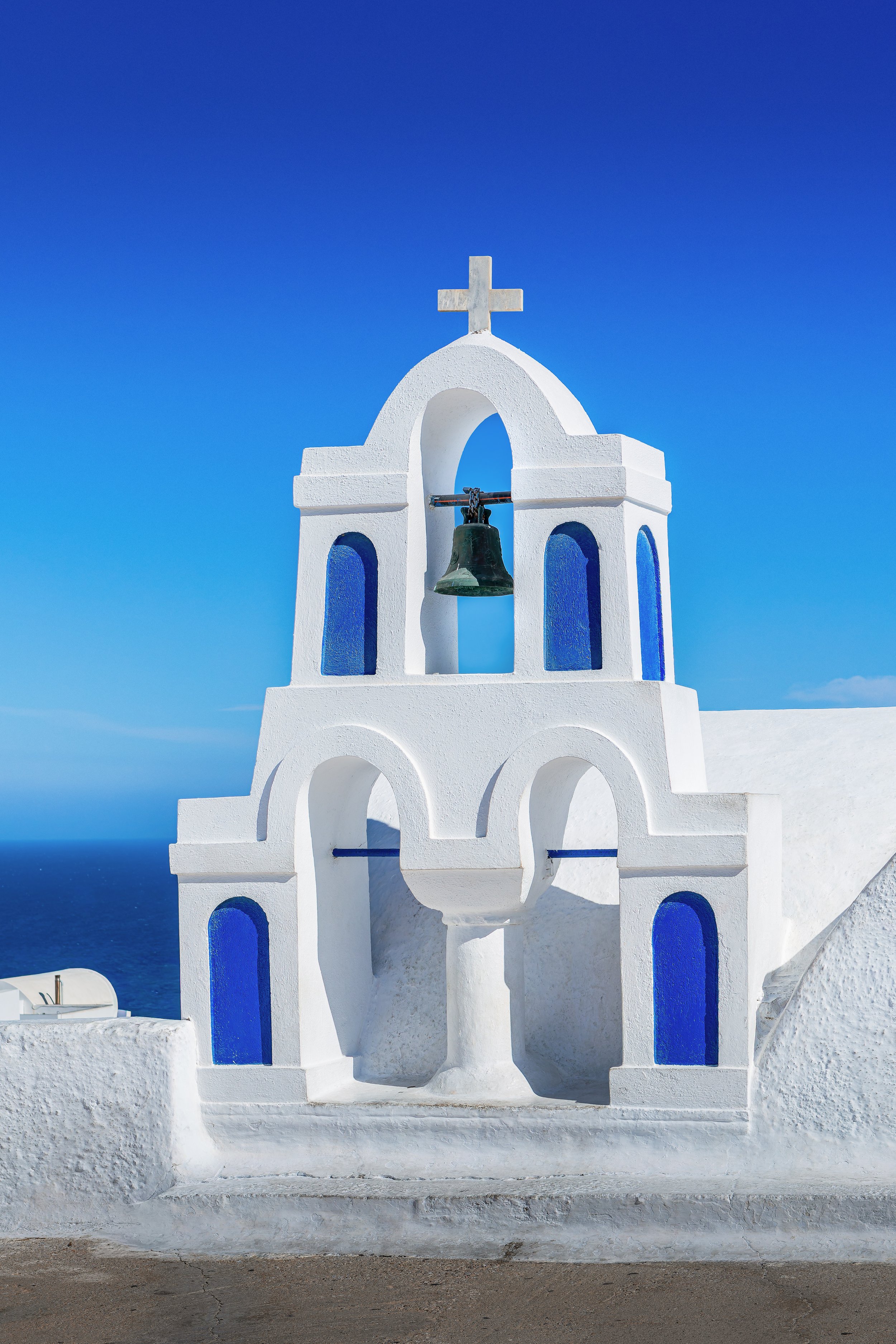 White bell tower with blue dome overlooking the sea in Santorini
