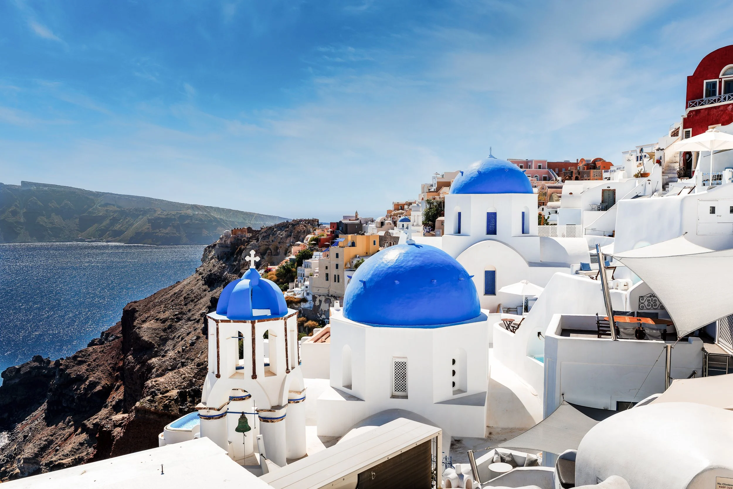 White buildings with blue domes on a hillside overlooking the Aegean Sea in Santorini, Greece.