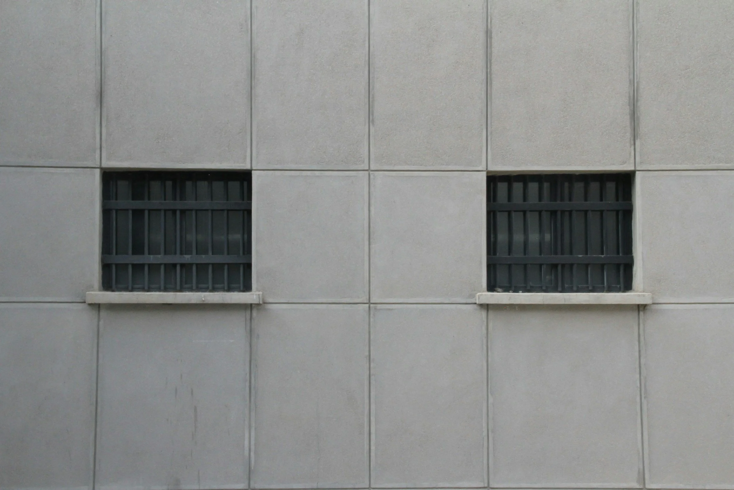 A gray concrete wall with two small, barred windows evenly spaced.