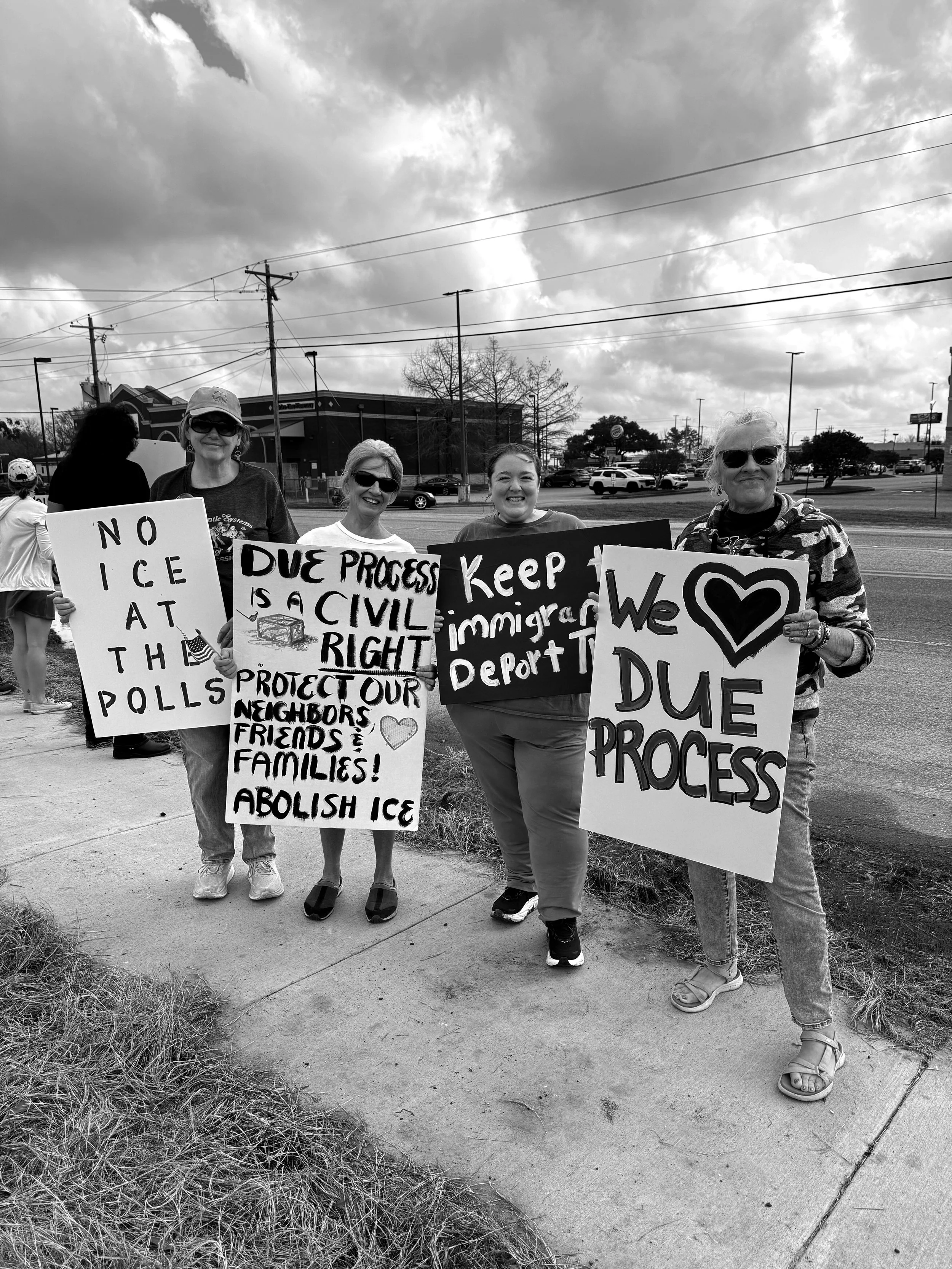 A group of five women holding protest signs in a parking lot under cloudy skies, advocating for immigrant rights, opposing ICE, and supporting DACA.