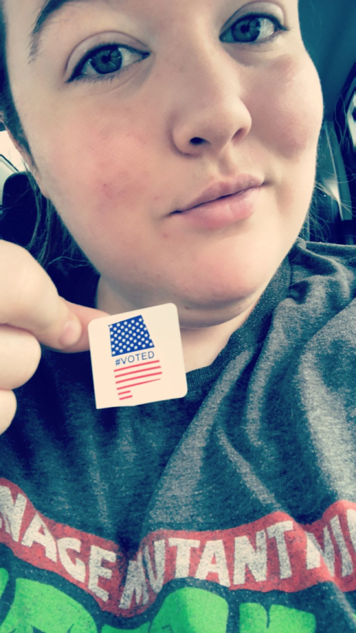 A woman holding an 'I Voted' sticker with patriotic colors near her face.