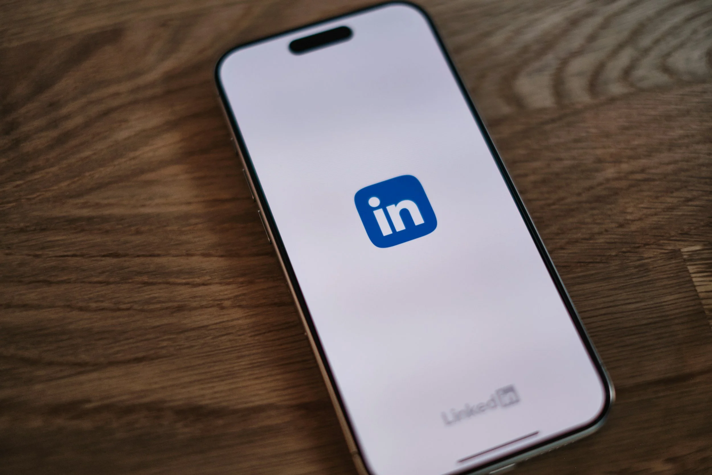 A smartphone displaying the LinkedIn app logo on the screen, resting on a wooden surface.