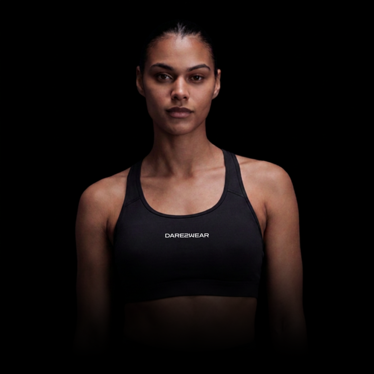 A woman in a black sports bra with 'DARE2WEAR' written on it, standing against a black background.
