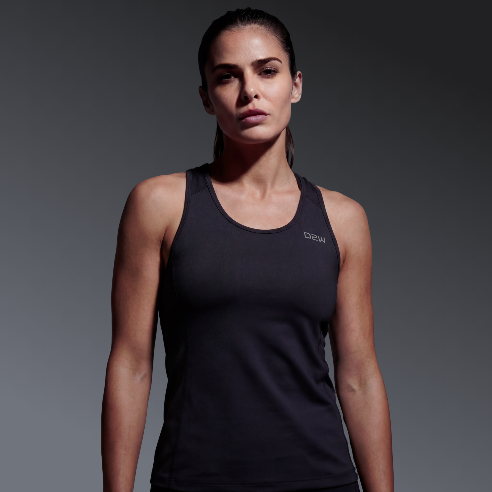A woman in a black athletic tank top standing against a dark gradient background.